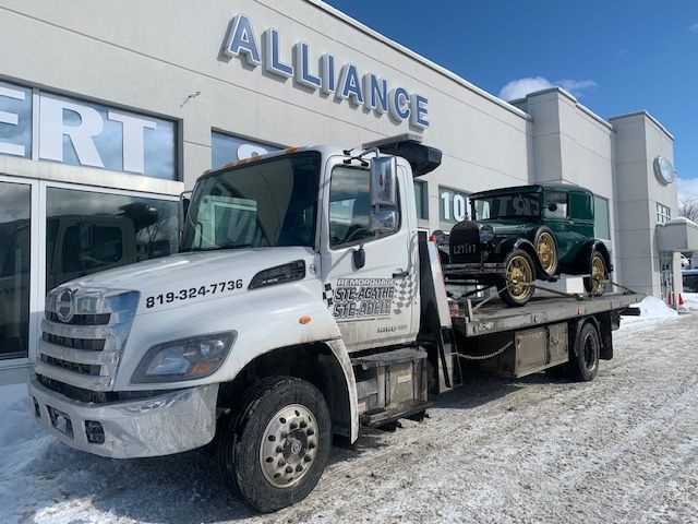 Une dépanneuse est garée devant un bâtiment sur lequel est écrit alliance