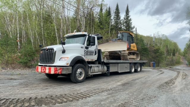 Une dépanneuse transporte un bulldozer sur un chemin de terre.