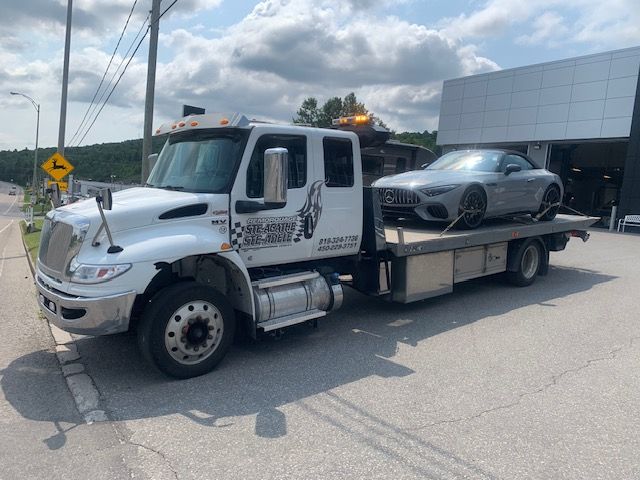 Une dépanneuse avec une voiture à l'arrière est garée sur le bord de la route.