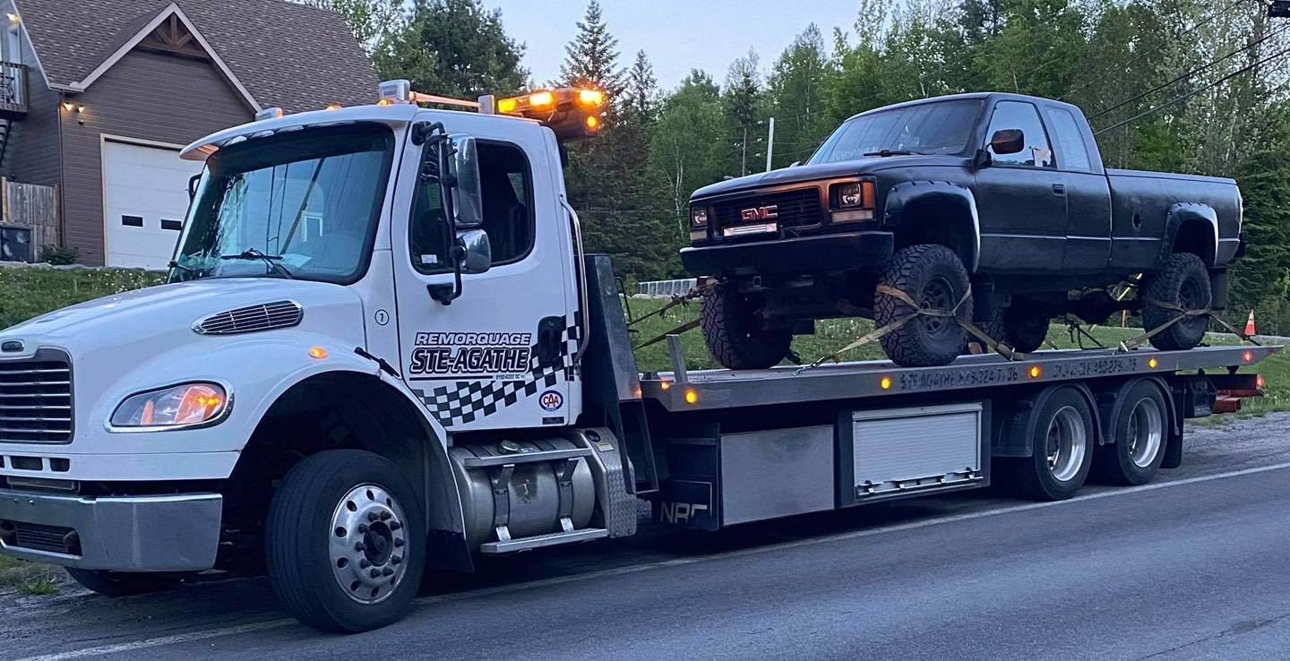 Une dépanneuse remorque un camion noir sur une remorque à plateau.