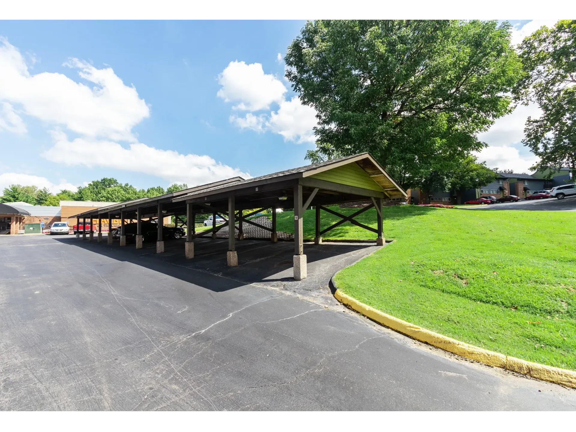 Covered carport with multiple parking stalls and cars beside a grassy slope.