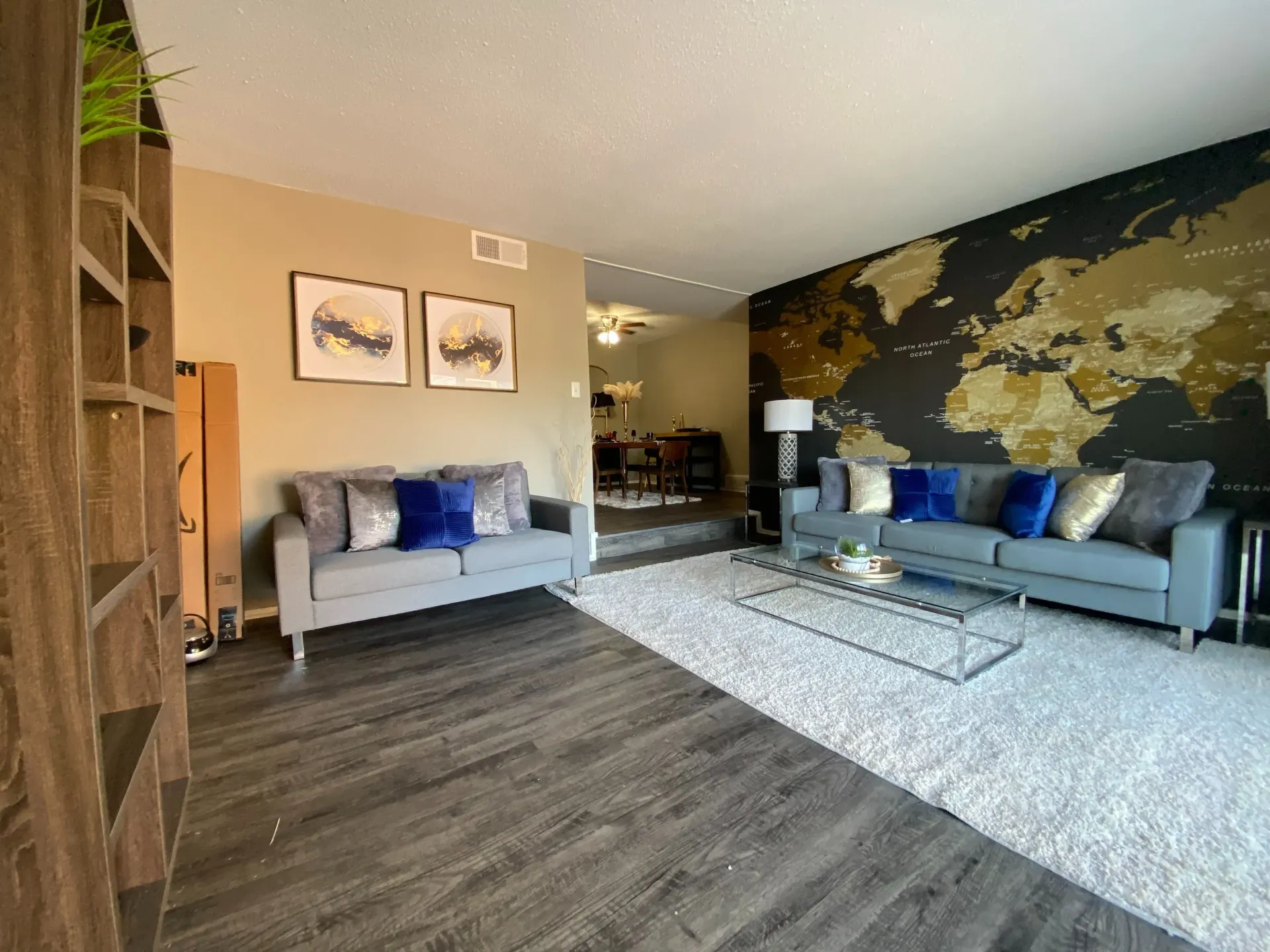 Living room in an apartment with two gray sofas, a glass coffee table, and a world map wall.