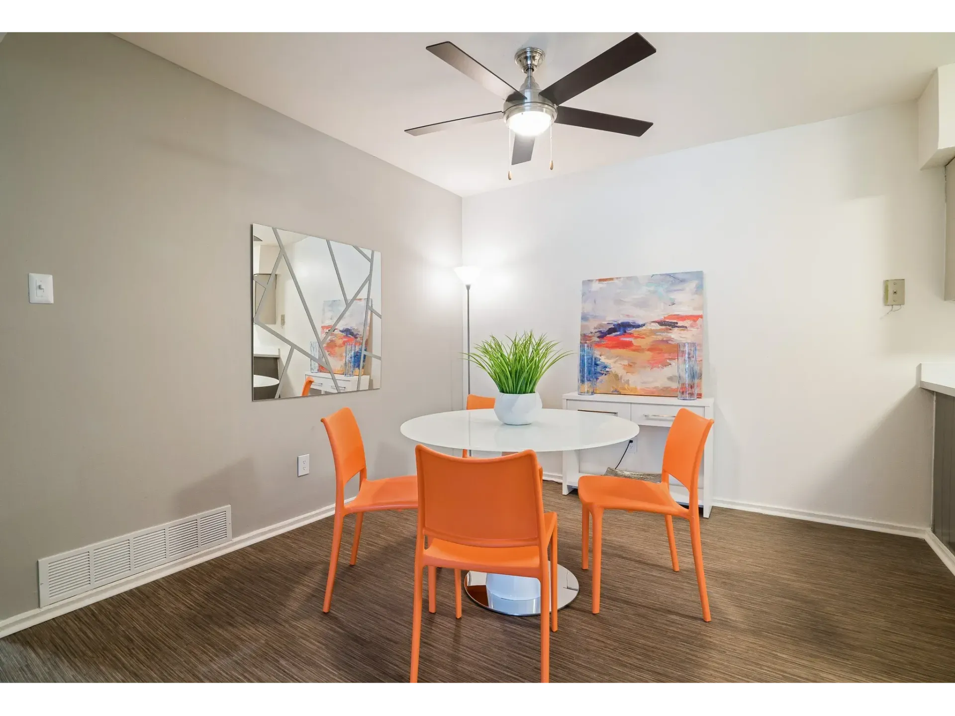 Dining area in a modern apartment with a round white table and orange chairs.