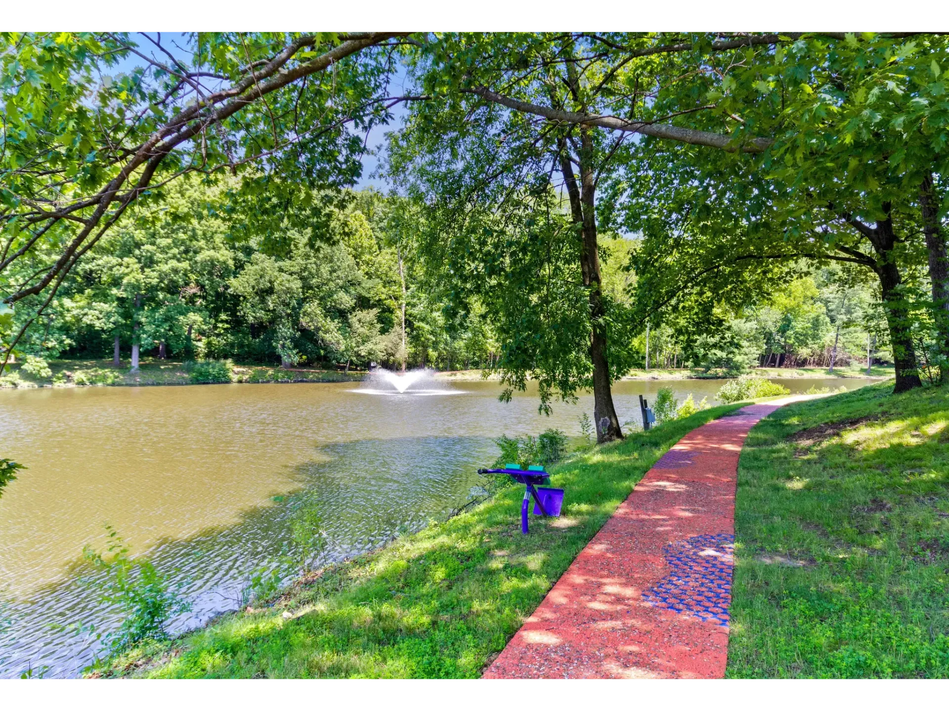 Serene lakeside view with a walking pathway and fountain in the background at Haven on the Lake in Maryland Heights, MO.