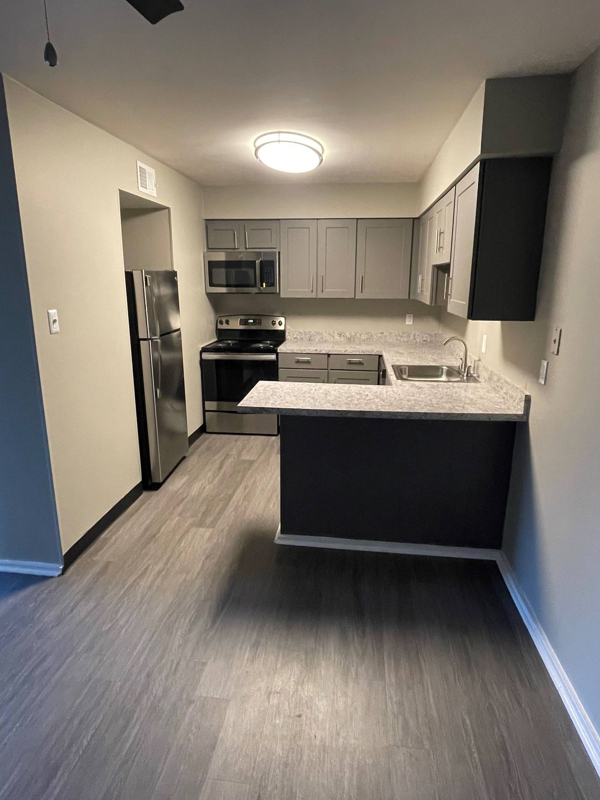 Modern apartment kitchen with gray cabinets, stainless steel fridge and appliances, and a countertop island.
