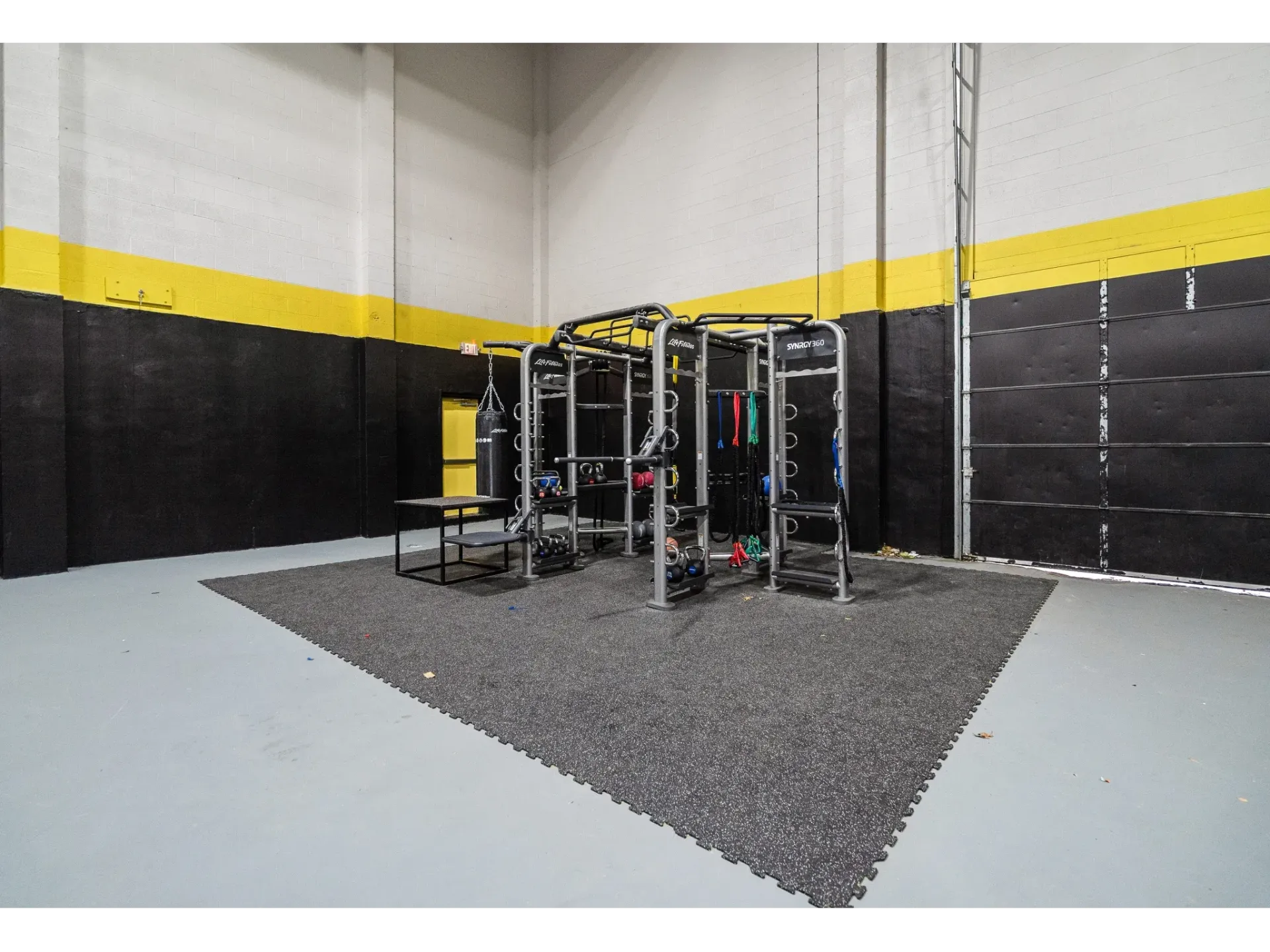 Indoor community gym with weight racks, mat area, and boxing bag.