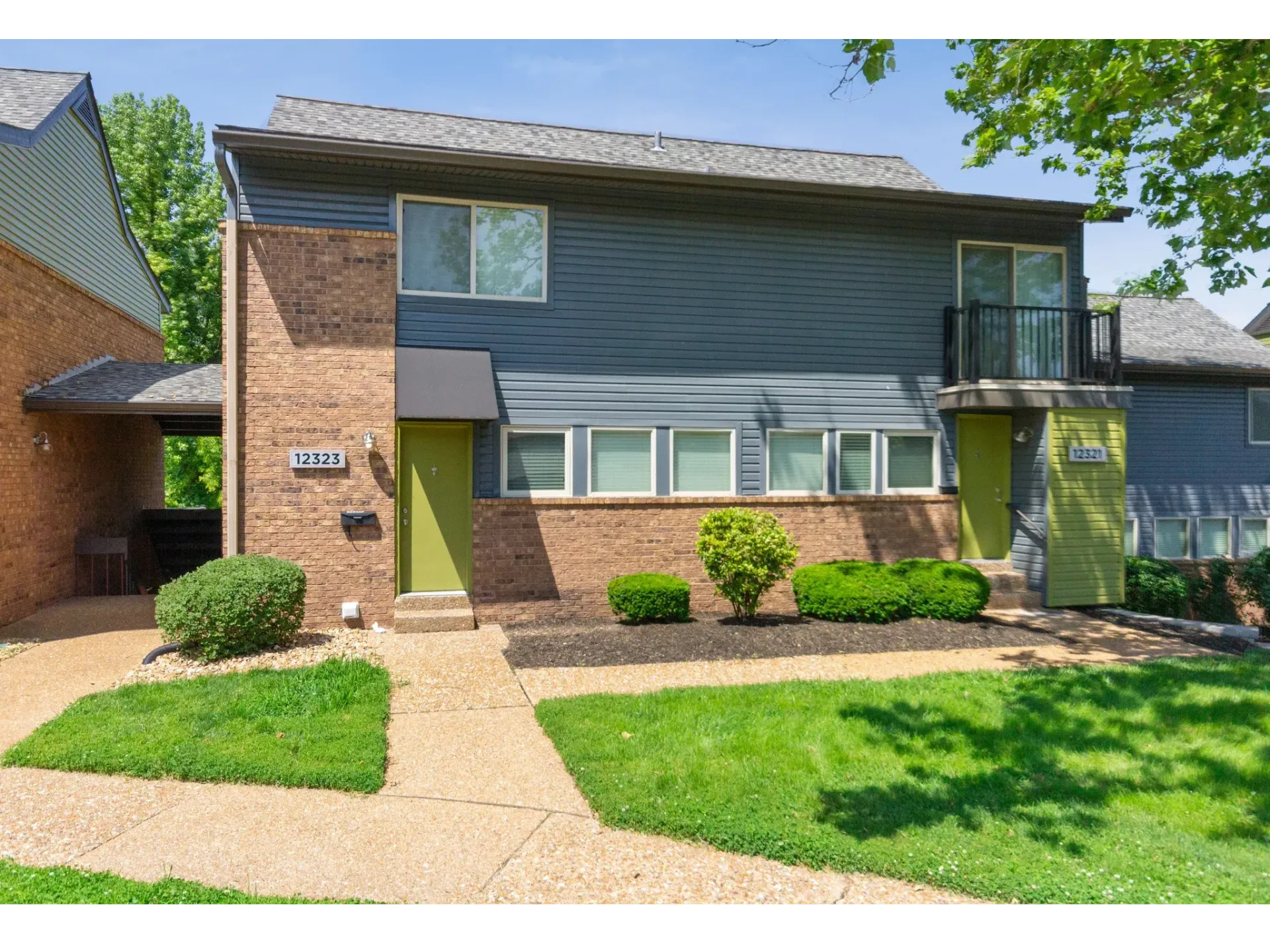 Two-story blue siding apartment building with brick accents and green entry doors, landscaped front.