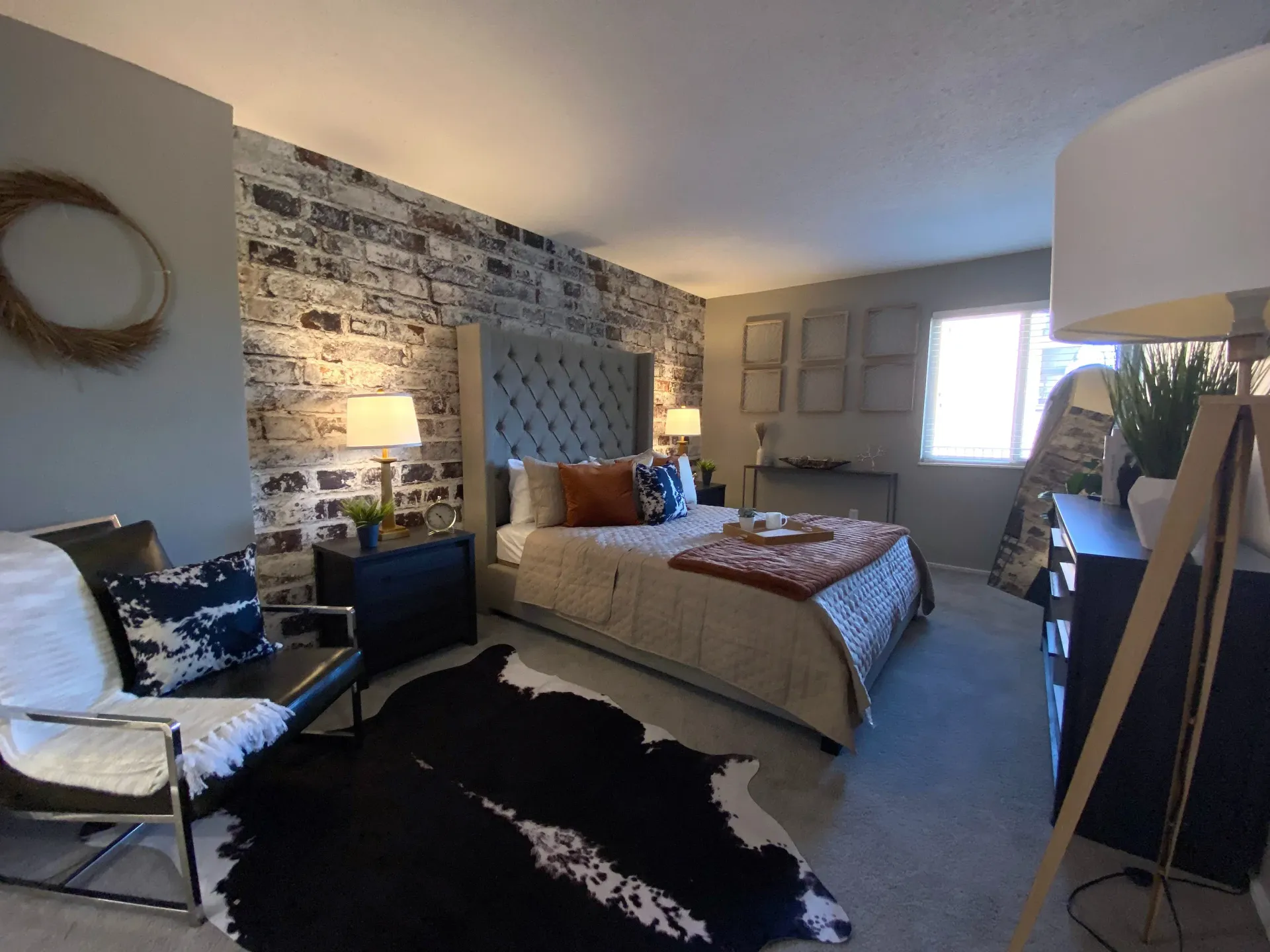 Bedroom in an apartment with a brick accent wall, tufted headboard, and modern furnishings.