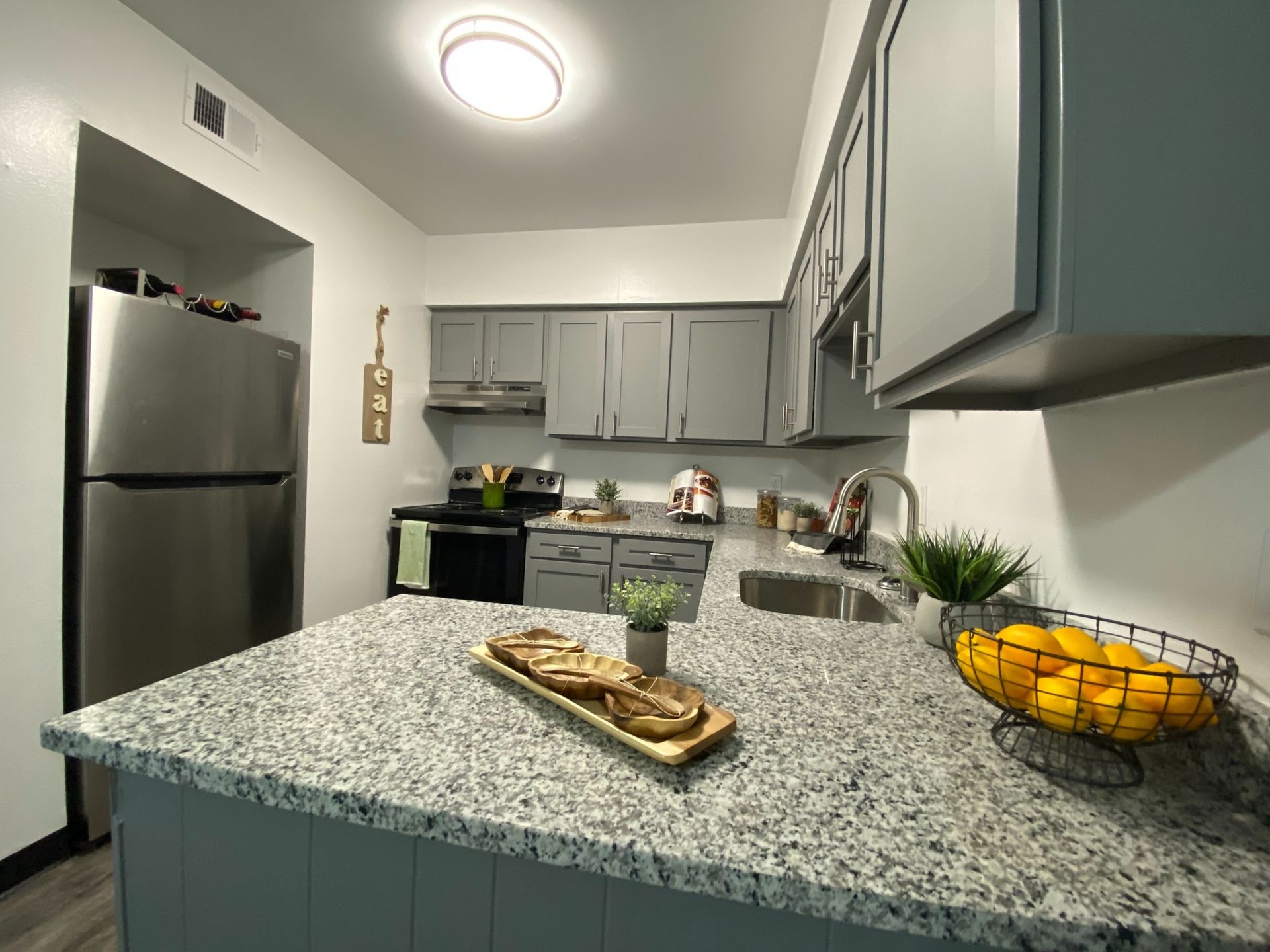 Modern apartment kitchen with gray cabinets, stainless steel fridge and stove, and granite countertops.