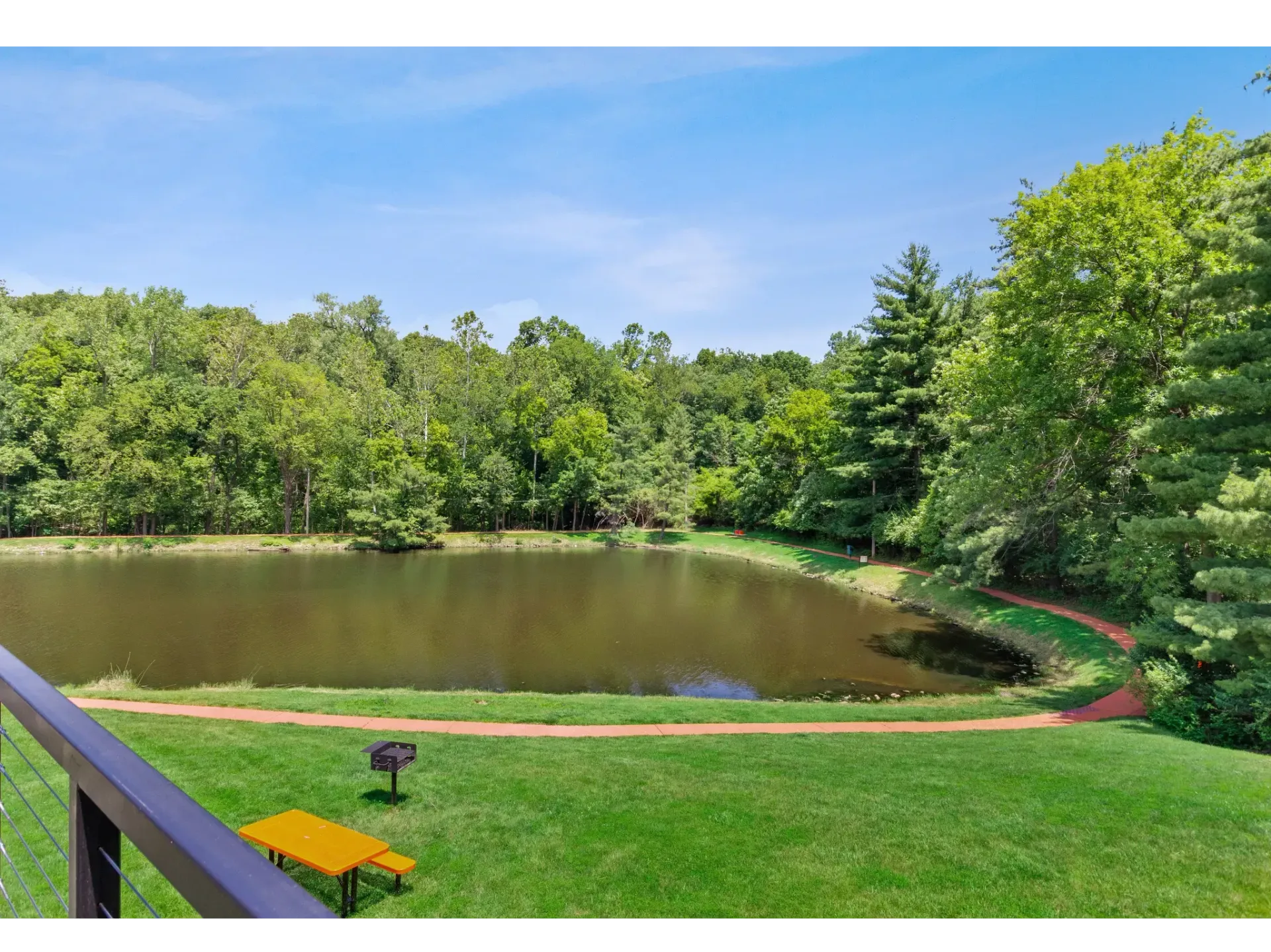 Scenic view of a pond surrounded by greenery and a walking path at Haven on the Lake in Maryland Heights, MO..