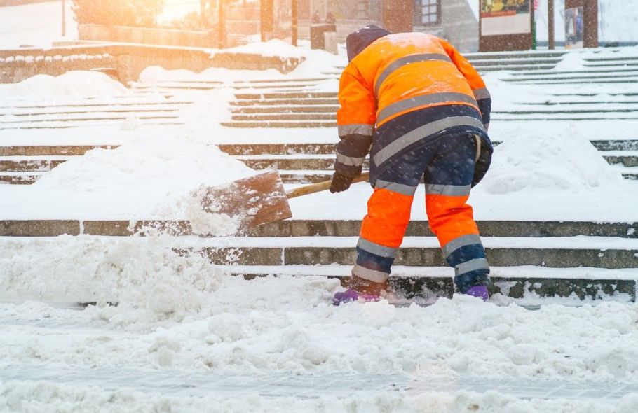Worker in orange safety jacket clearing snow from railroad tracks at sunrise