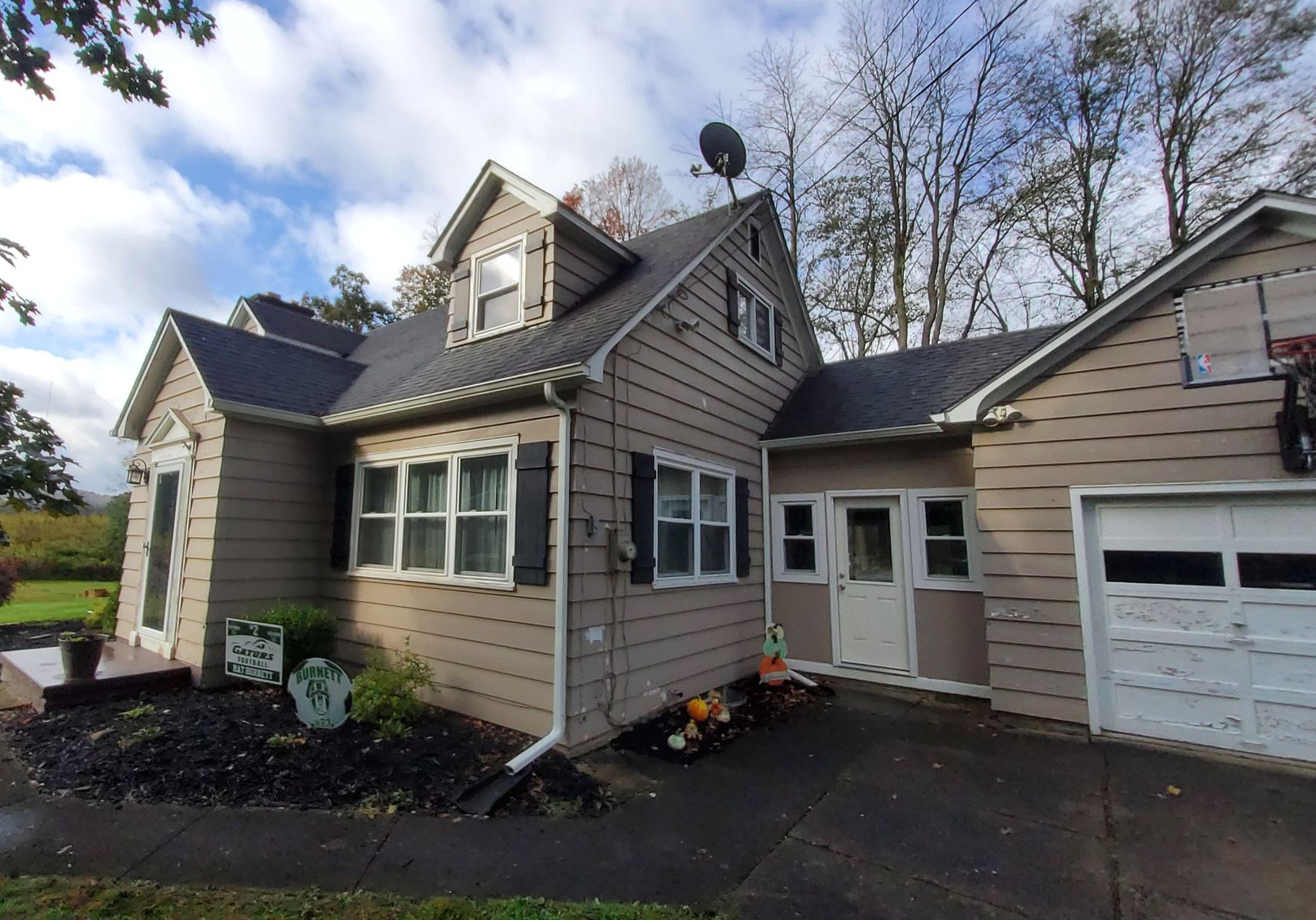 Tan house with a dark roof and garage, blue sky, and autumn foliage.