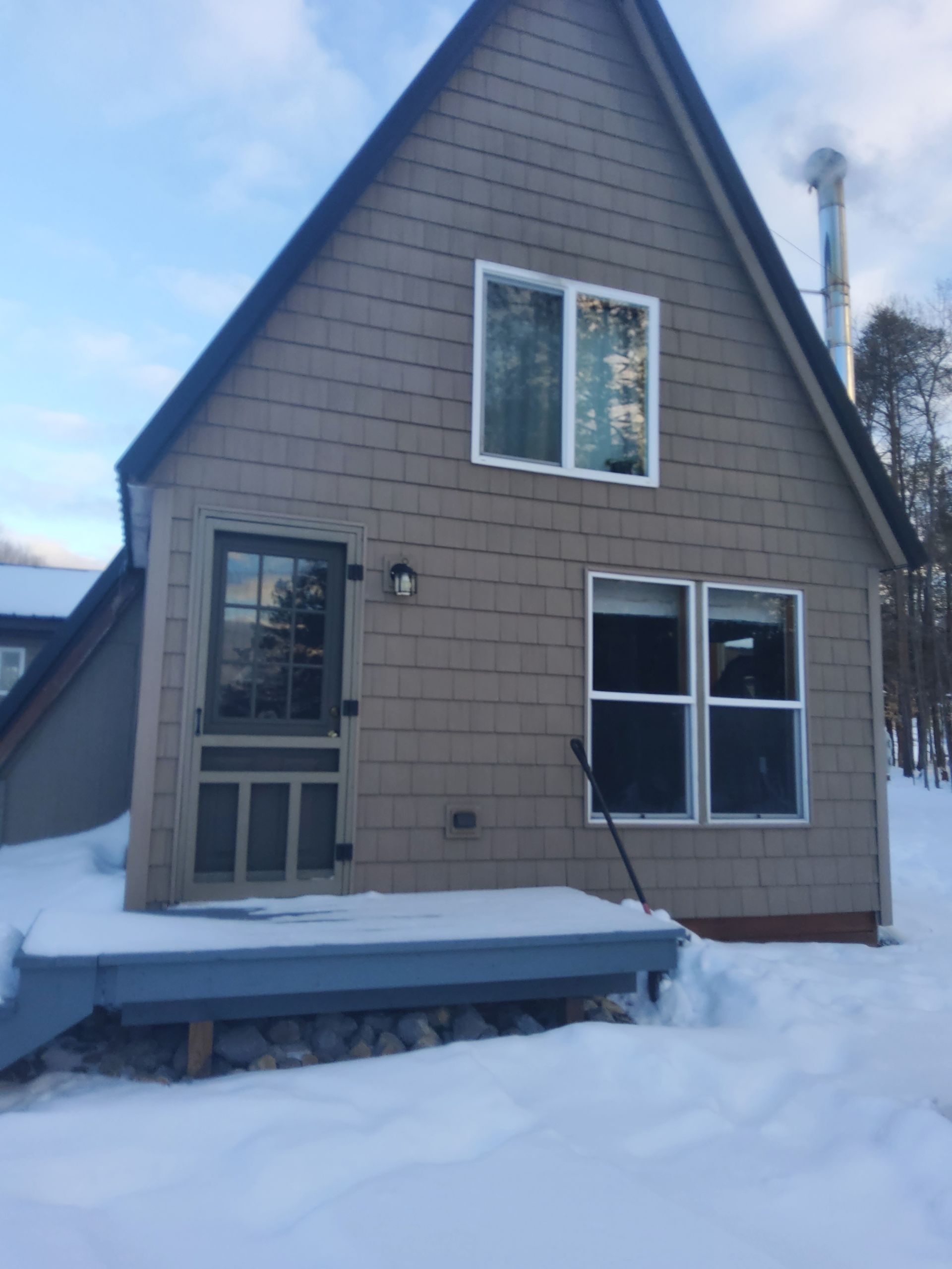 A-frame cabin covered in snow with a dark door, windows, and light siding.