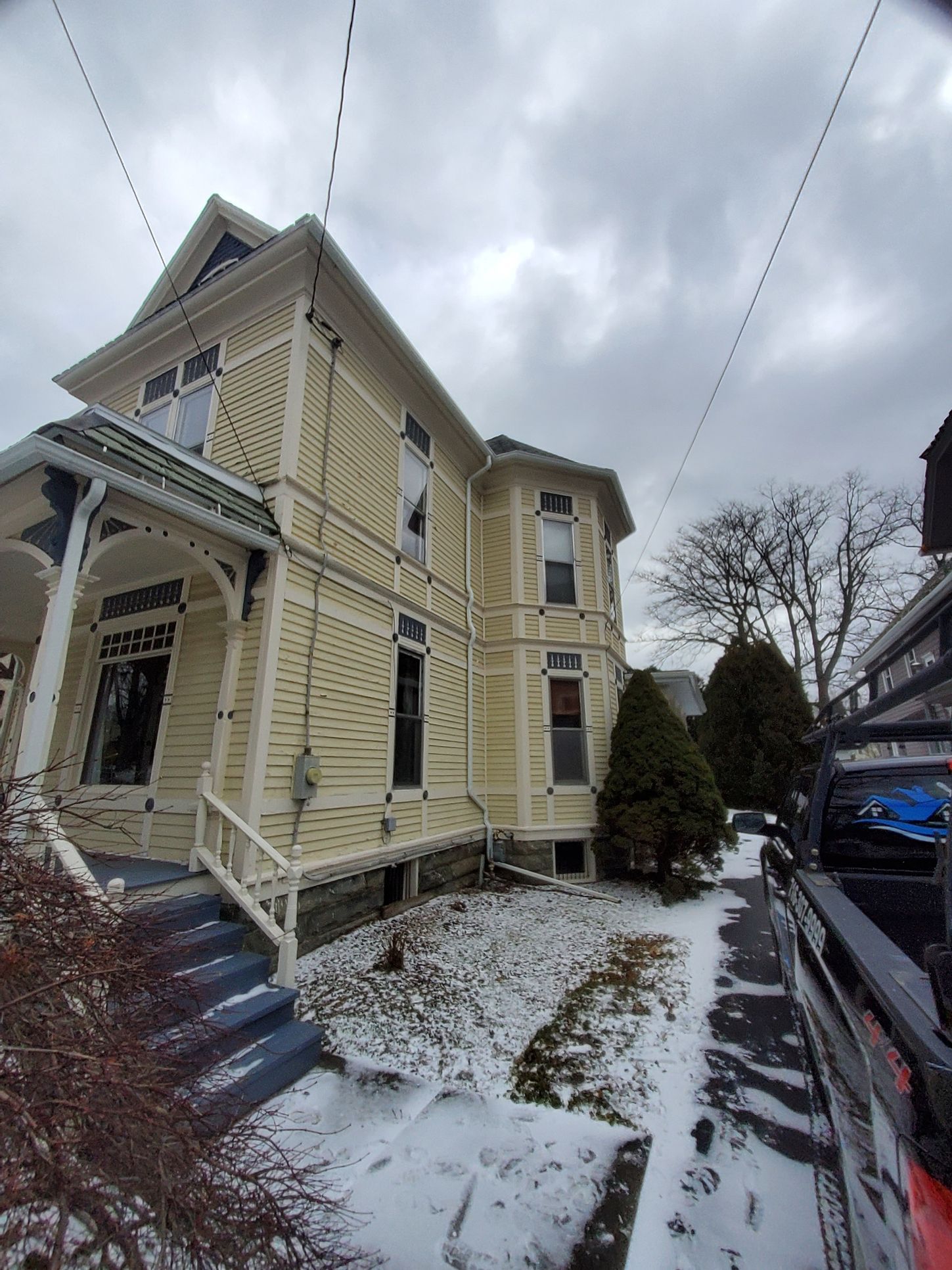 Yellow Victorian house with snow, front porch, and utility lines.