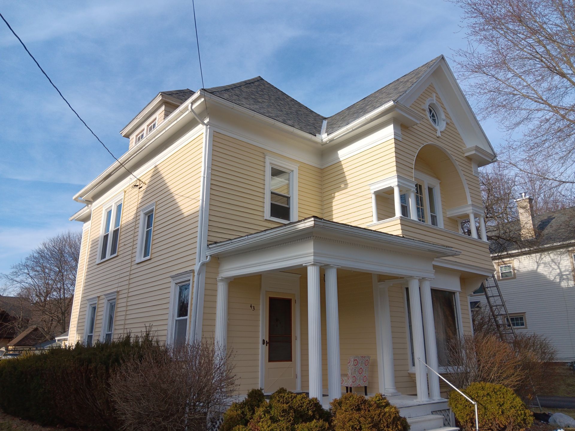 Yellow two-story house with a porch and dark roof, set under a blue sky.