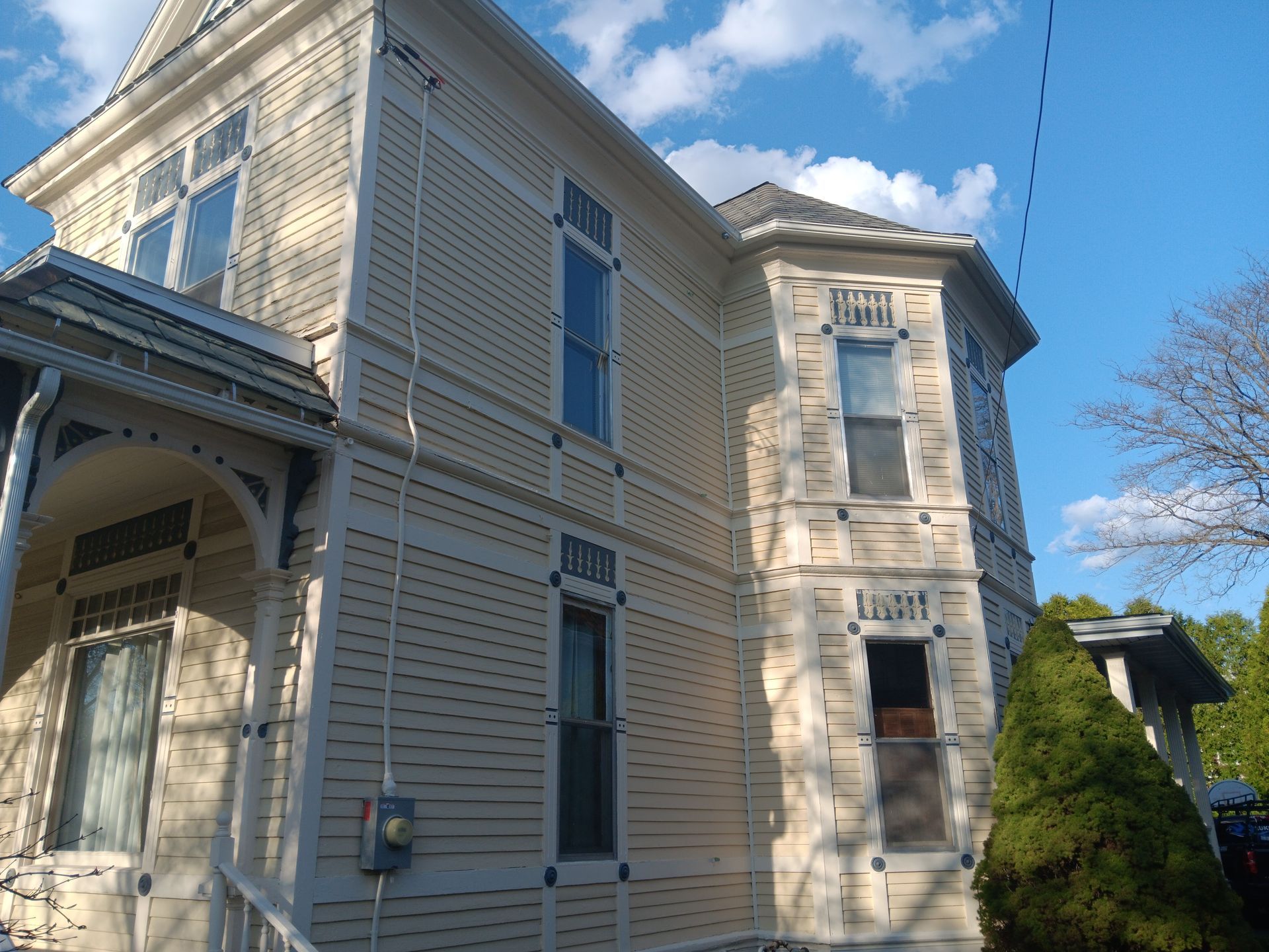 Victorian-style house with light yellow siding and intricate trim against a blue sky.