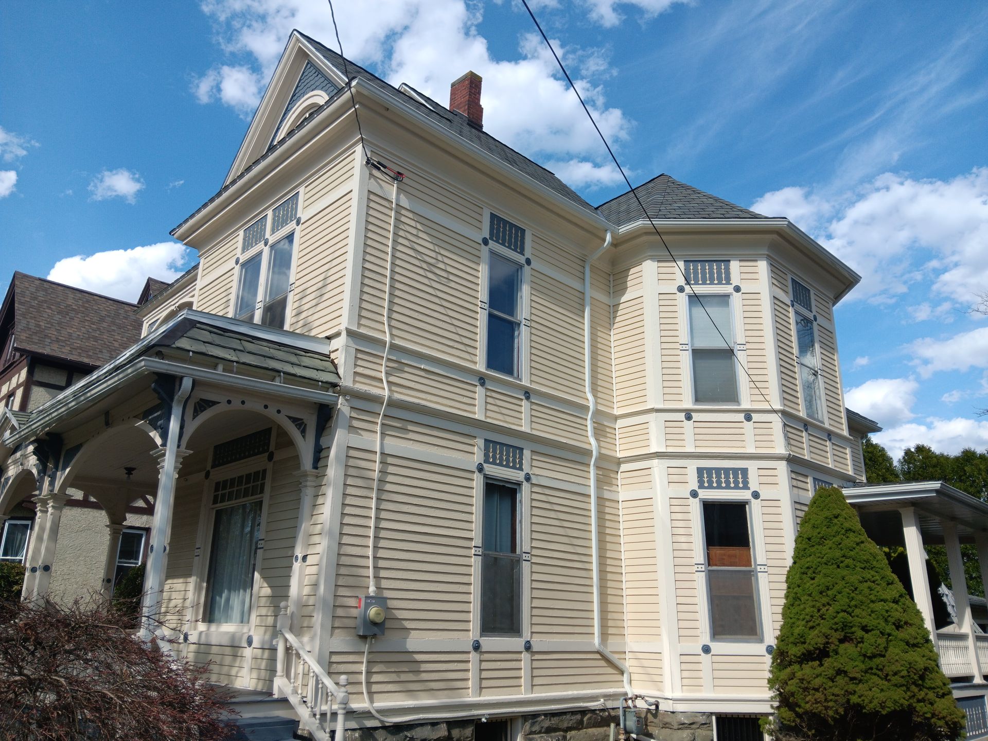 Victorian-style house with light yellow siding and intricate trim against a blue sky.