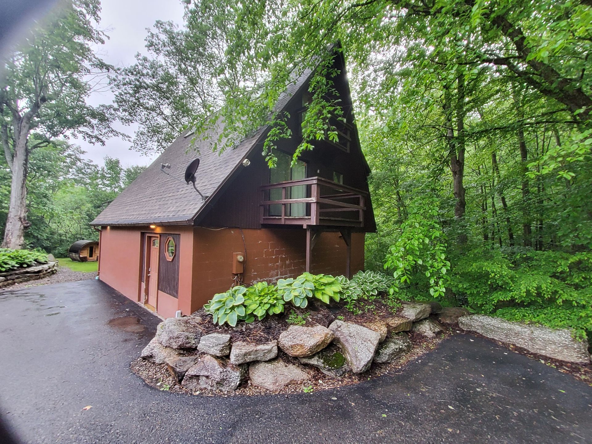 Brown A-frame cabin with a balcony and surrounding lush greenery.