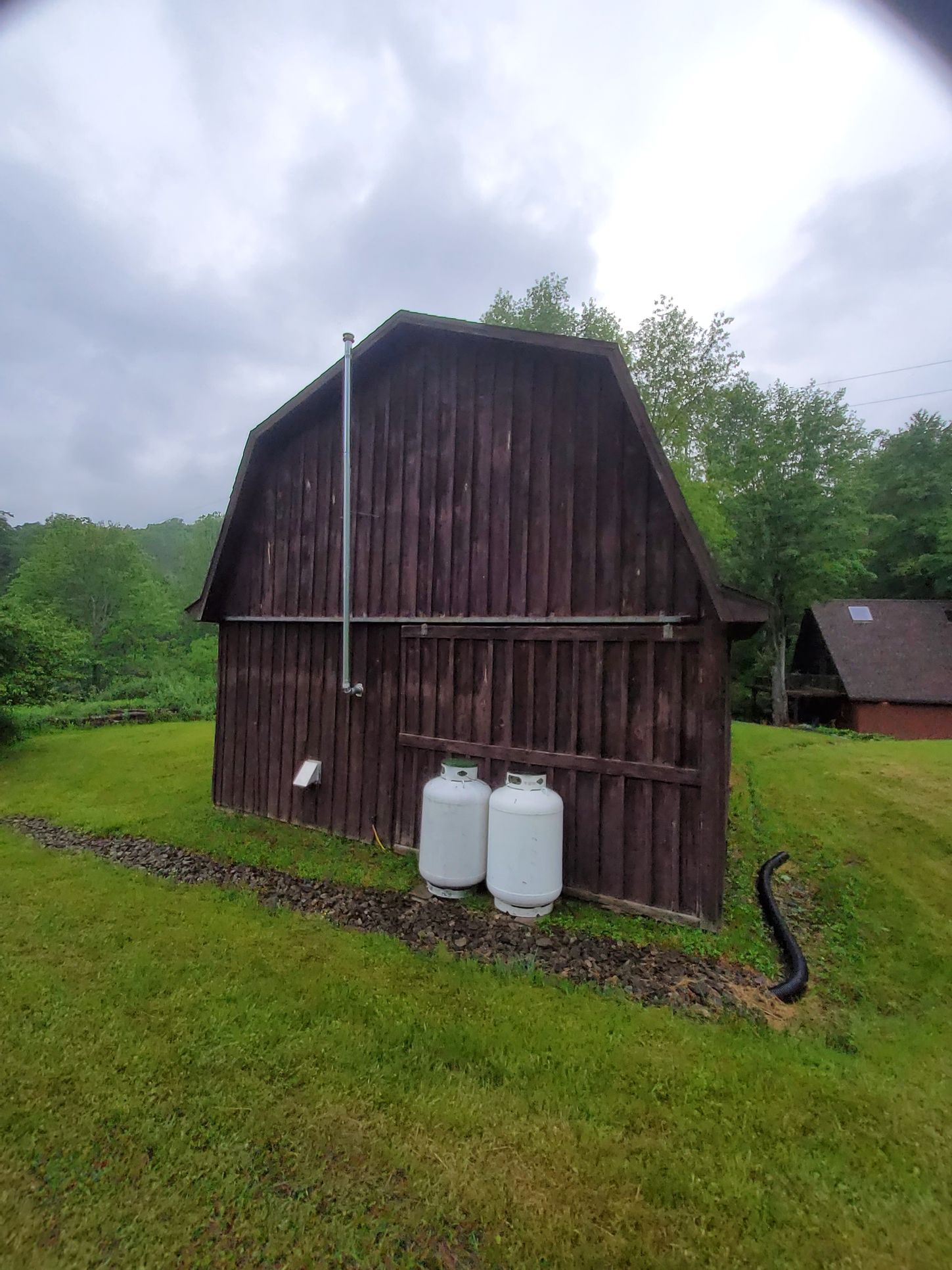 A brown barn with propane tanks outside, green grass, and overcast sky.