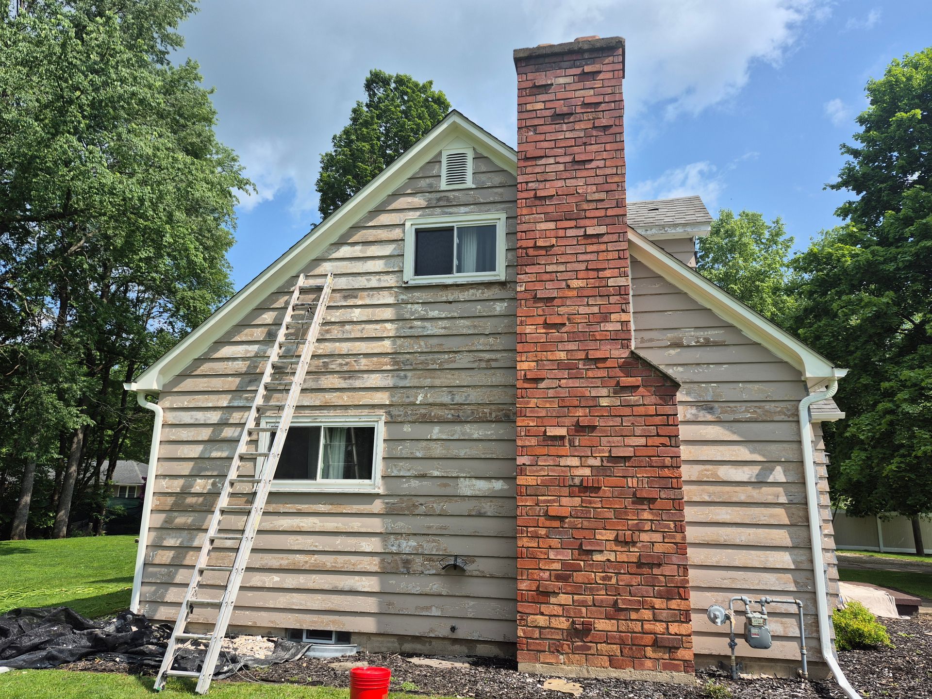 House exterior with ladder, peeling paint on siding, brick chimney, blue sky.