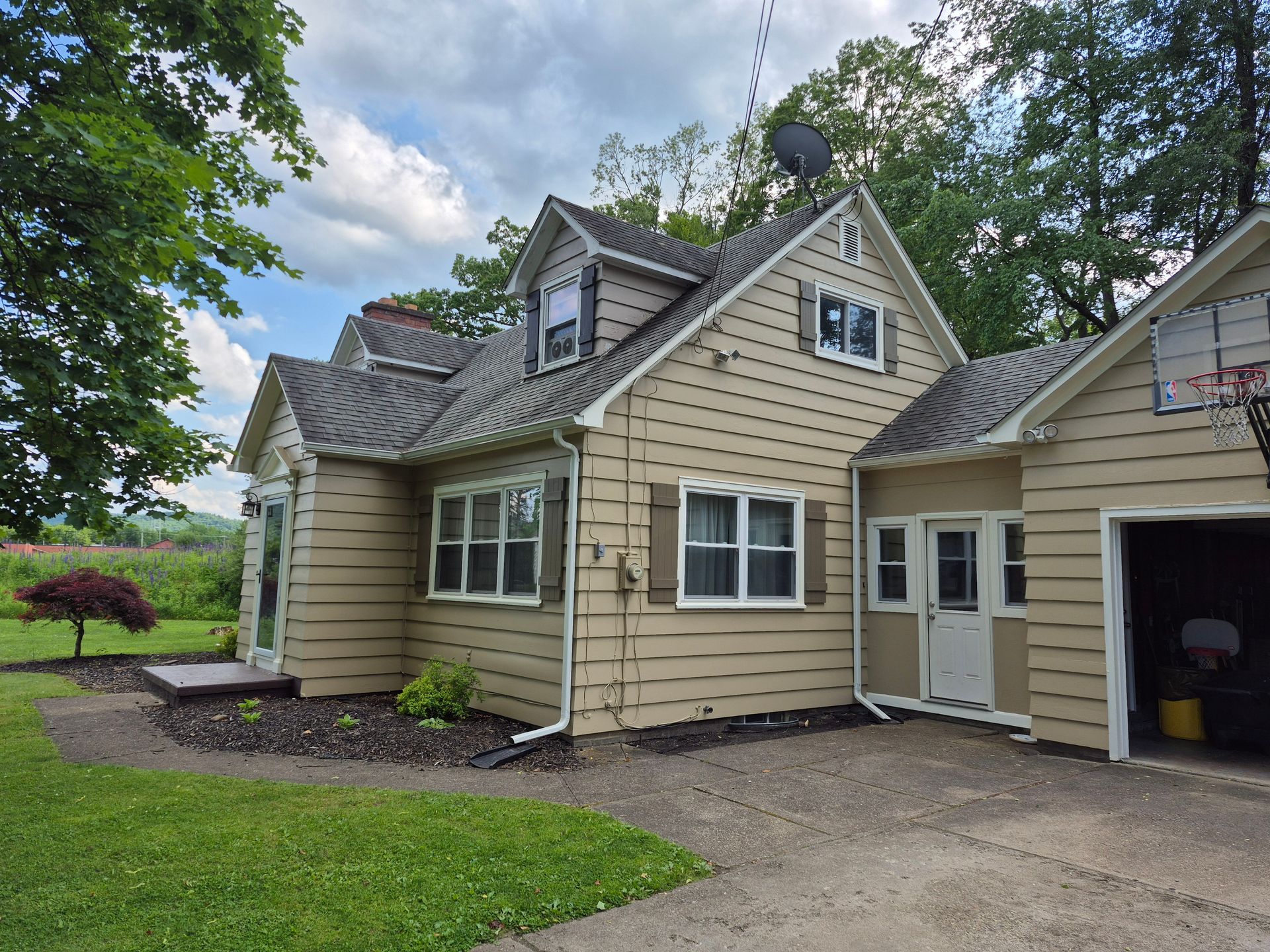 Beige-colored house with garage, dormer, and green lawn; driveway.