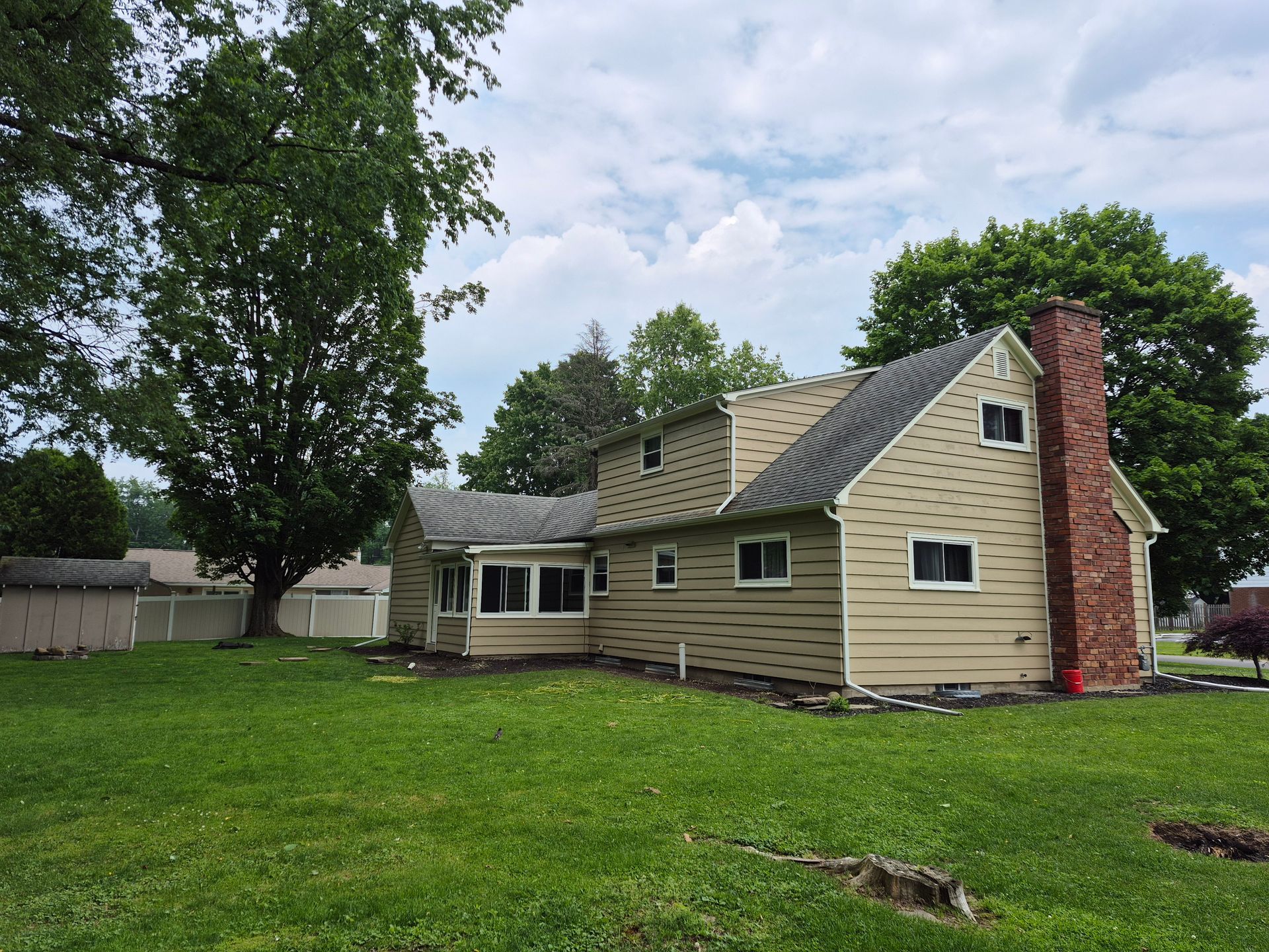 Beige two-story house with a brick chimney and green lawn. Overcast sky.