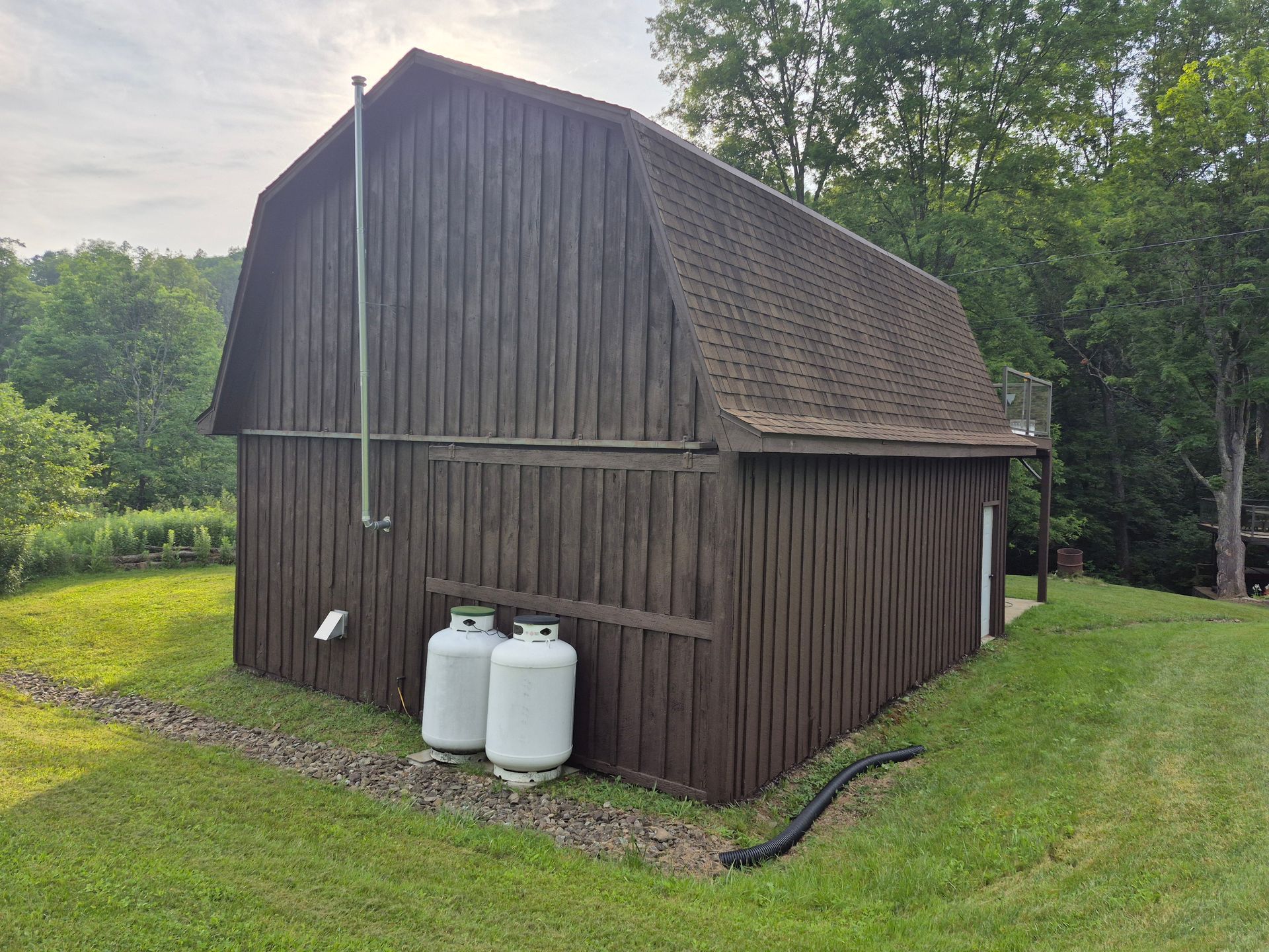 Brown barn with propane tanks on a grassy hillside.