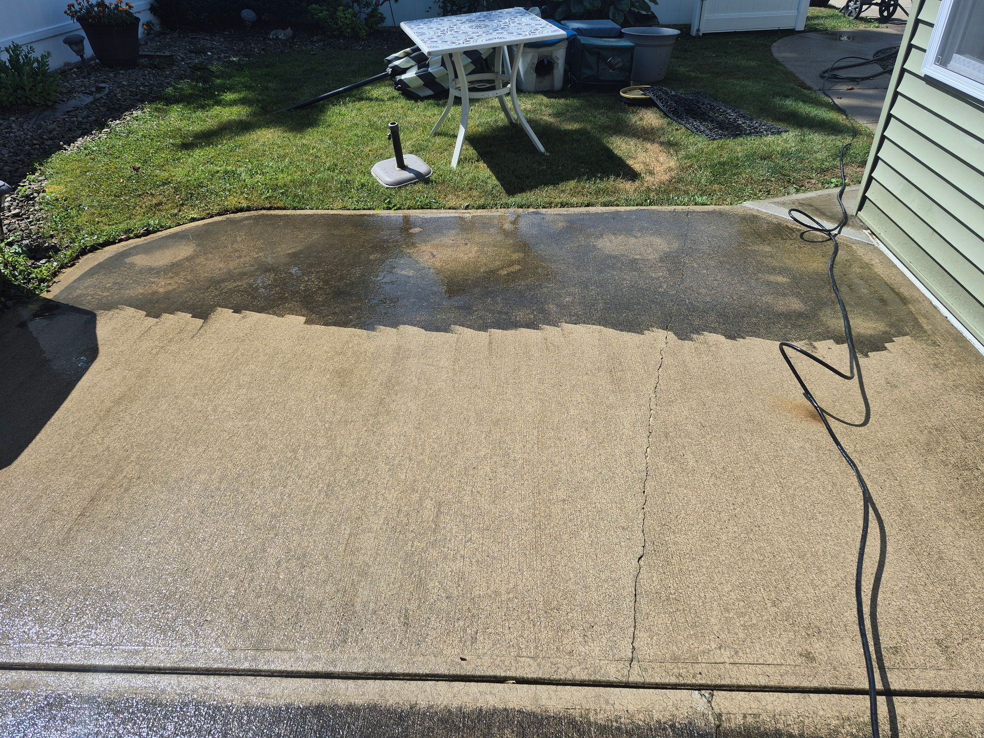 A concrete patio being power washed, with a bright lawn and house siding visible.