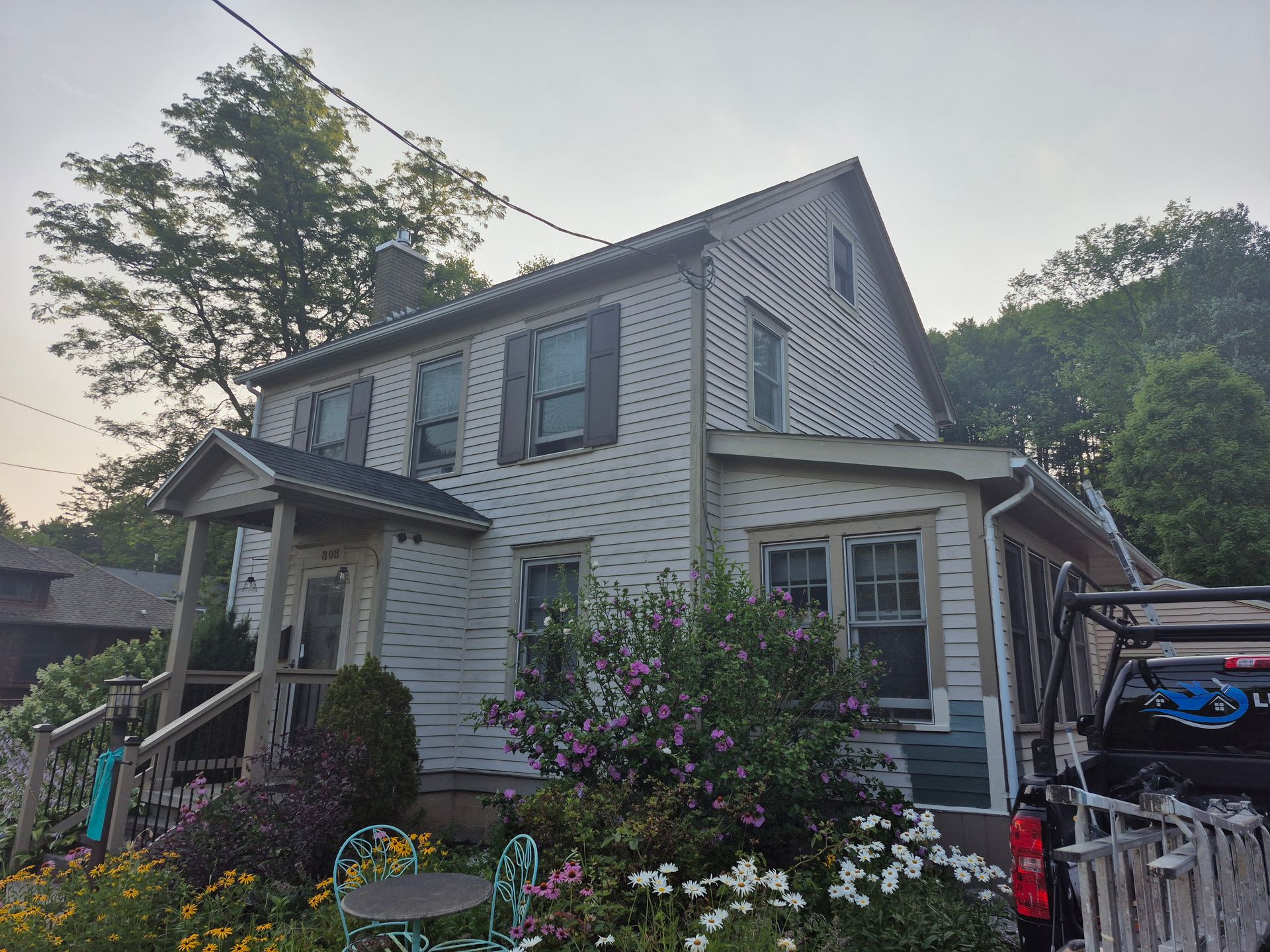 Two-story house with white siding and a porch, surrounded by a garden with flowers.