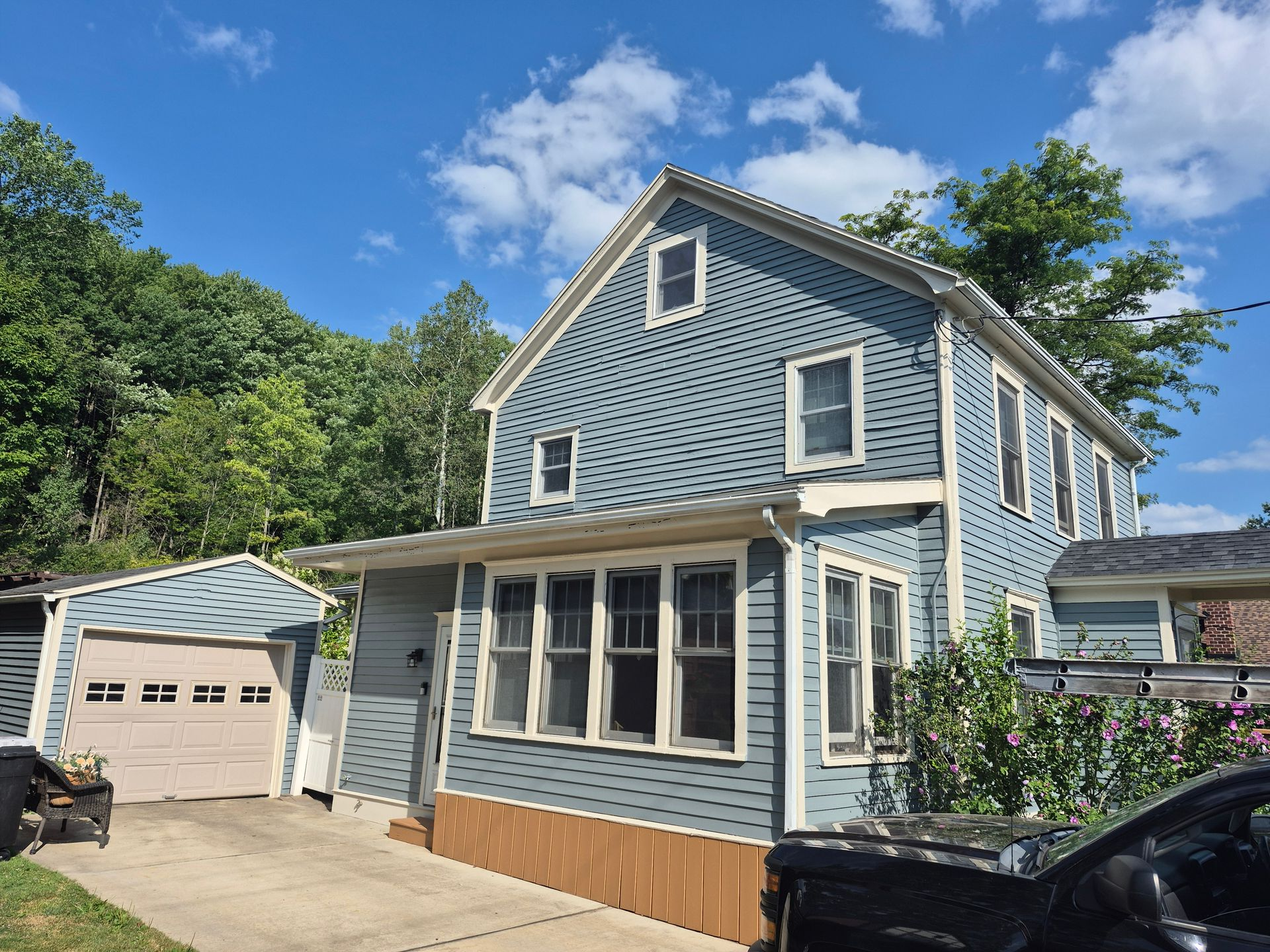 Two-story blue house with attached garage, windows, and brown trim against a blue sky.