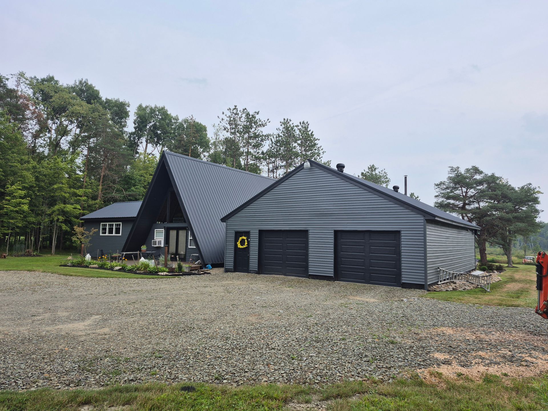 A-frame house and garage with dark gray siding and roof, set on a gravel driveway.
