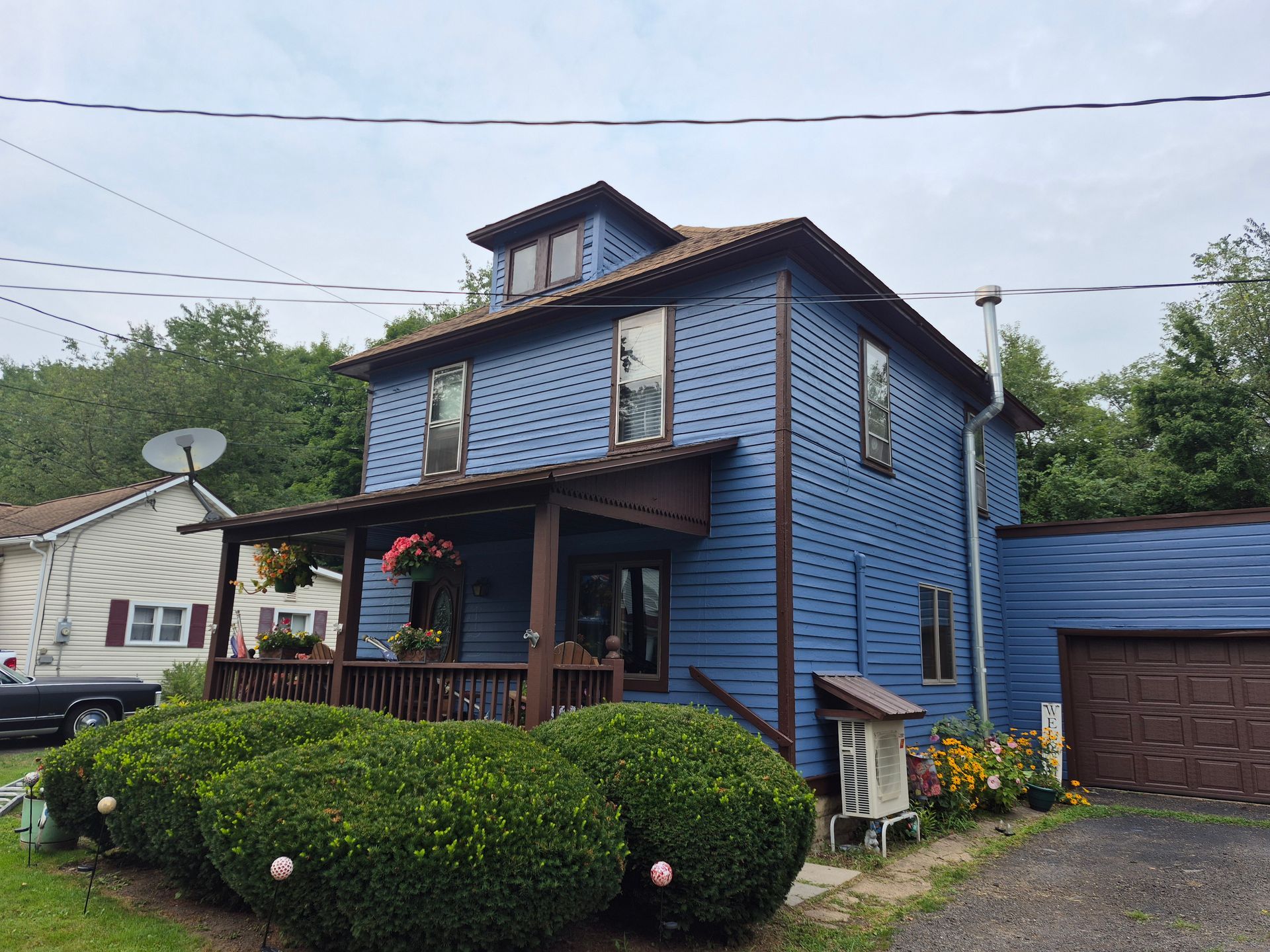 Blue house with porch, shrubs, and a side garage, under cloudy sky.
