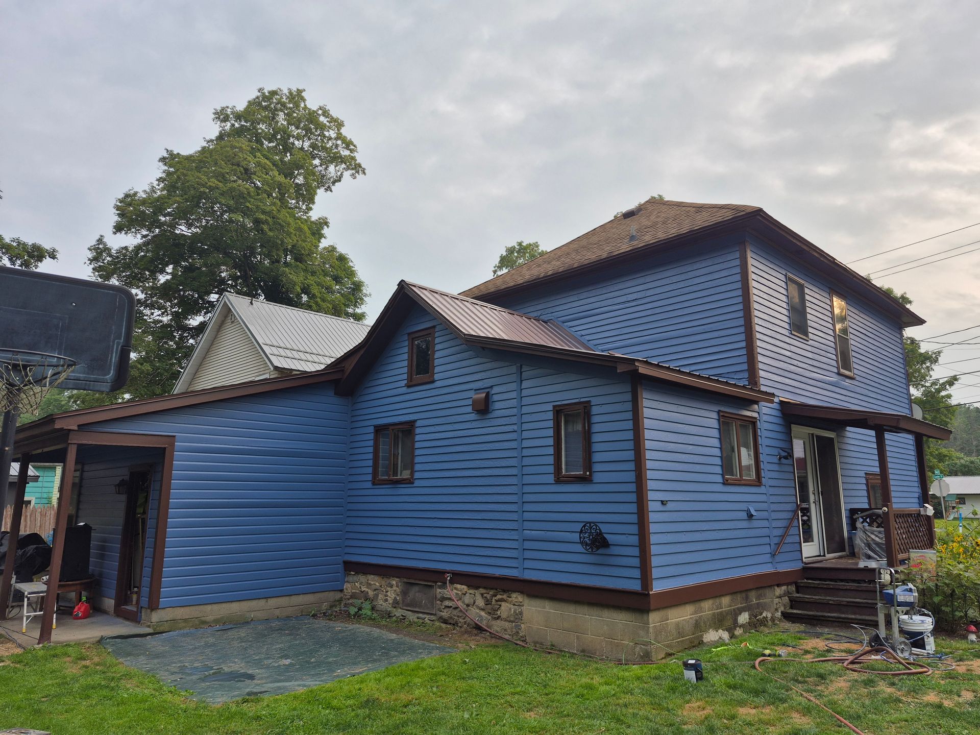 Blue house with brown trim and metal roof, on a cloudy day.