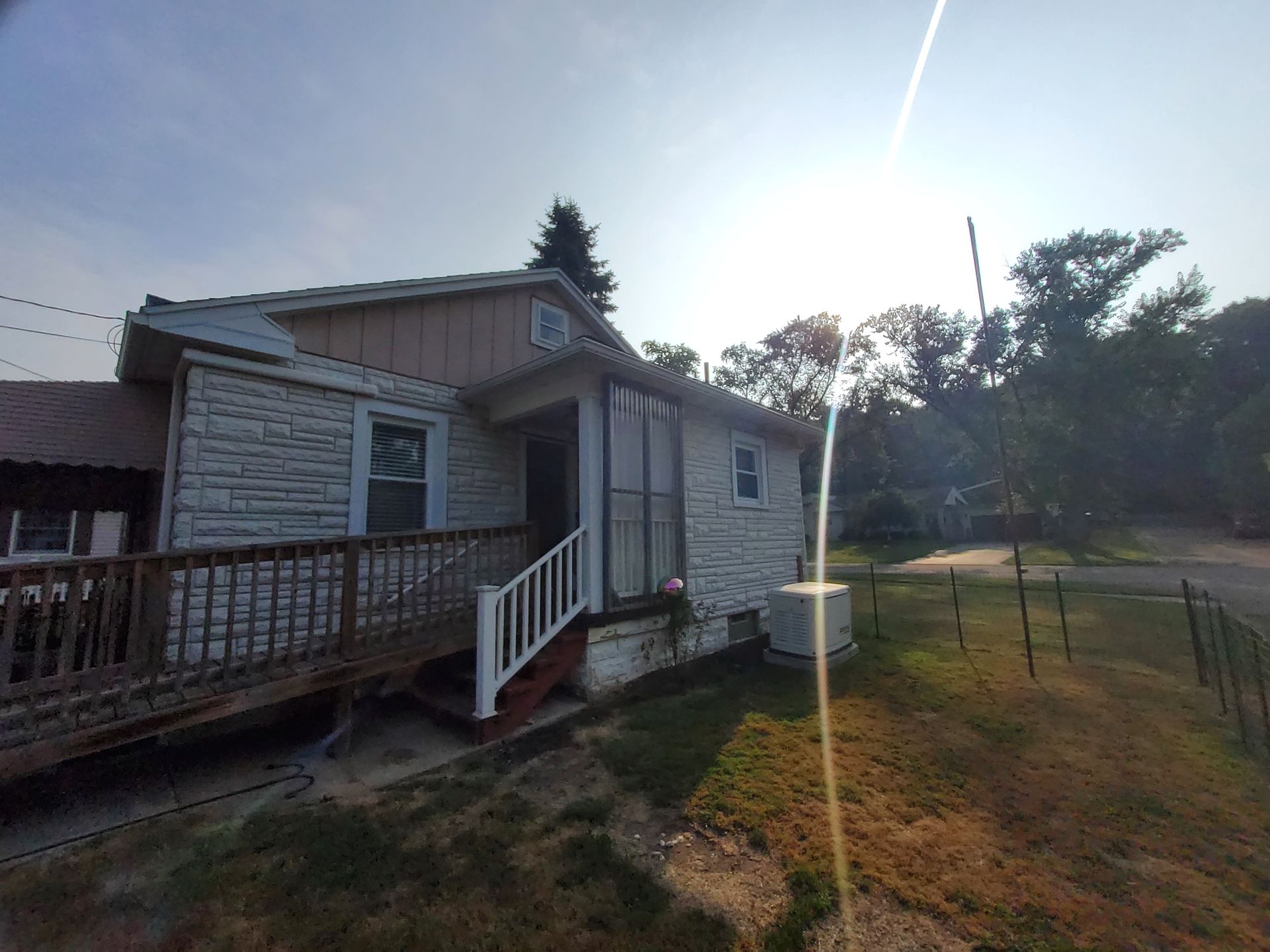 House with stone facade, wooden deck and ramp. Sunny outdoor setting.