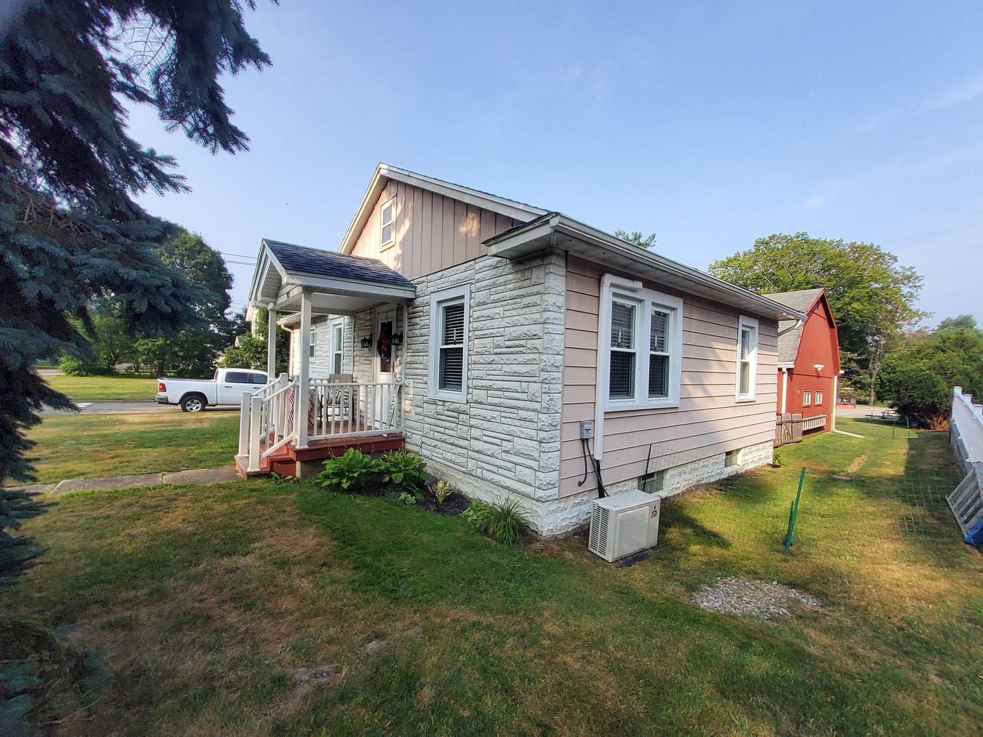 Small house with stone facade, pink siding, porch, and red door. Green grass and blue sky.
