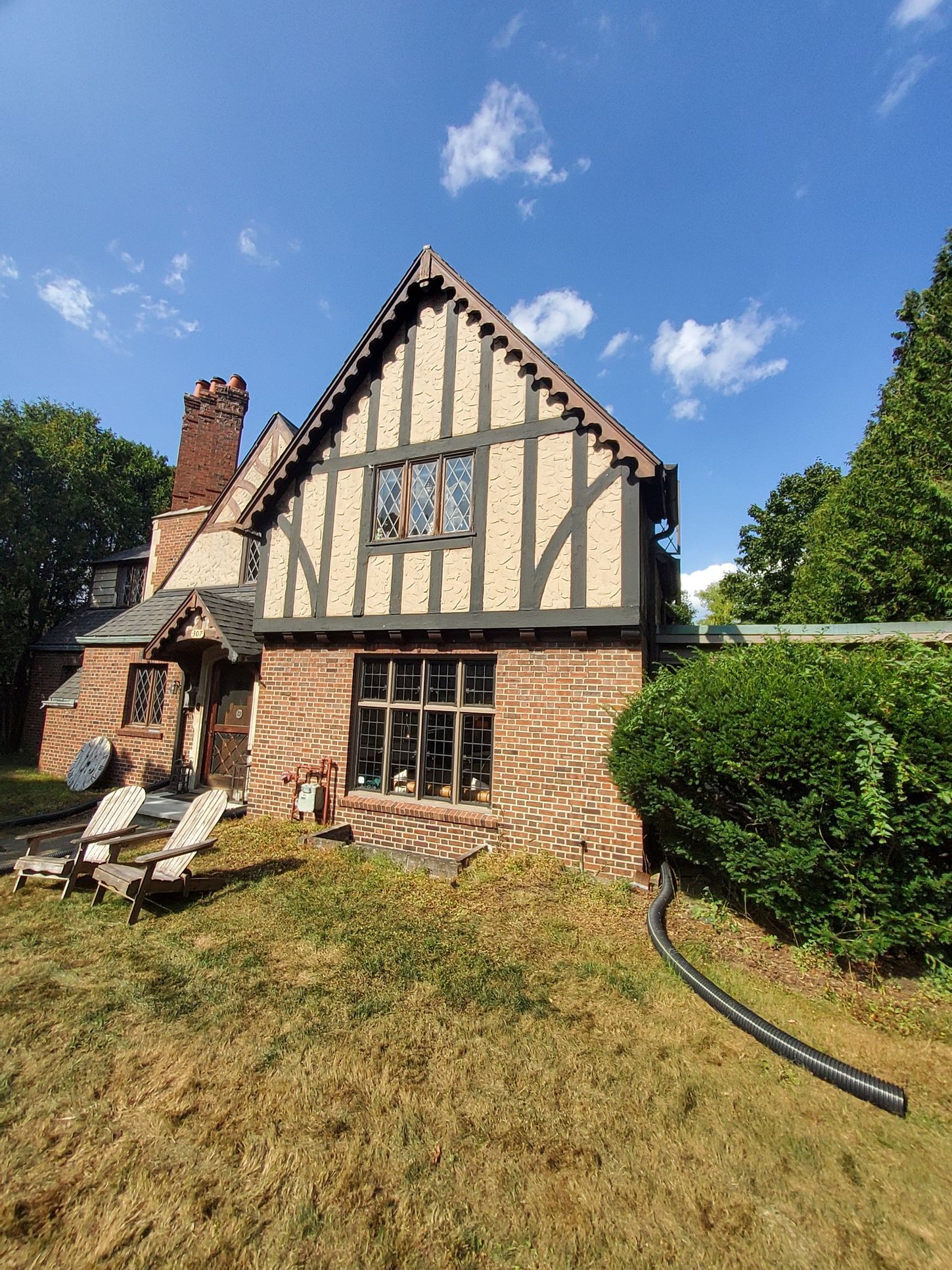 Tudor-style house with brick and dark wood trim, set on a lawn under a blue sky.