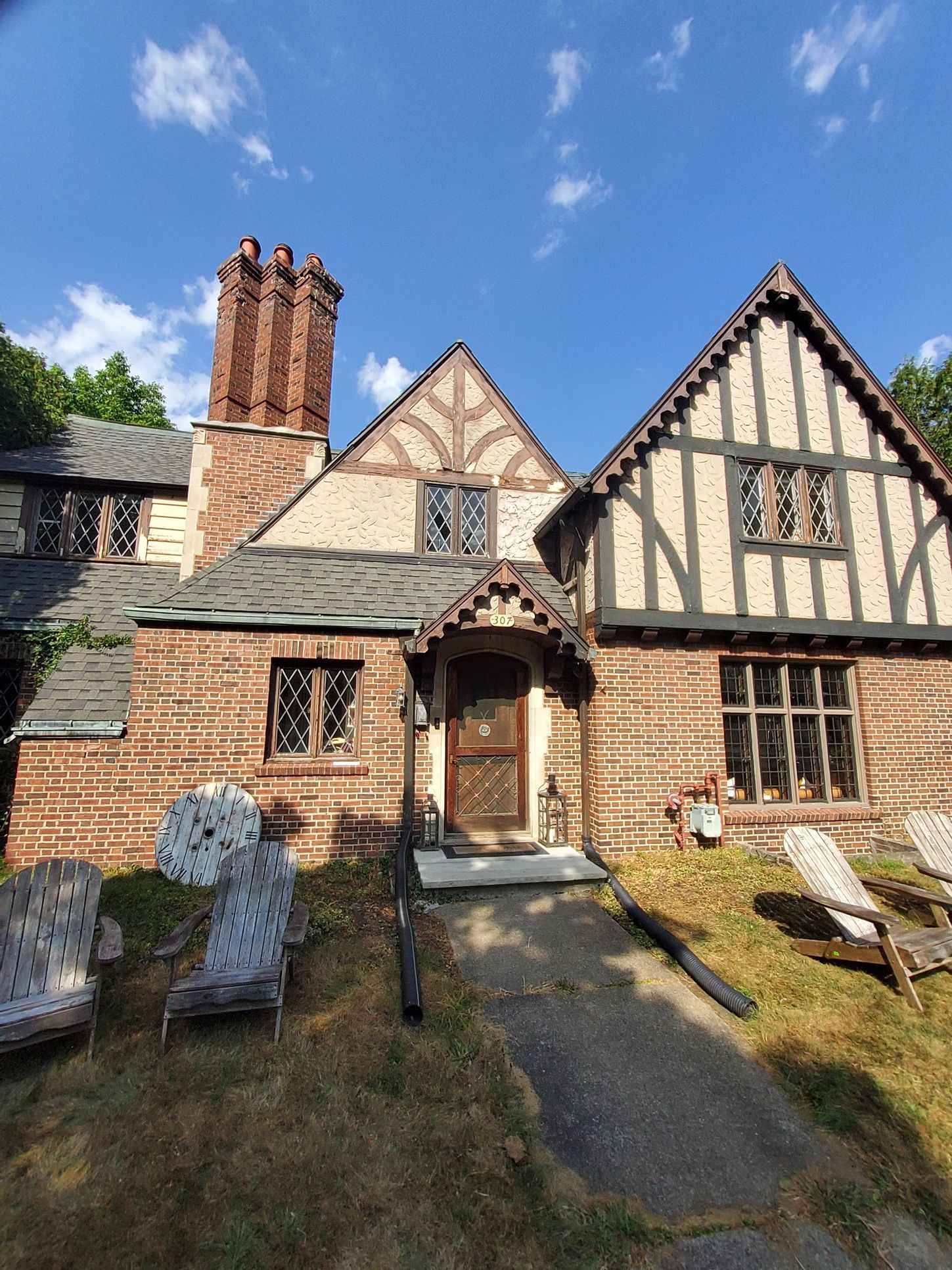 Tudor-style brick and timber house with multiple gables, arched windows, and a tall brick chimney.