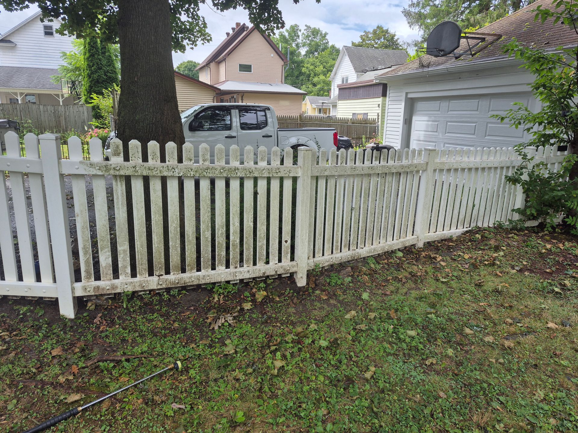 White picket fence with algae, in front of a house, and a truck parked behind the fence.