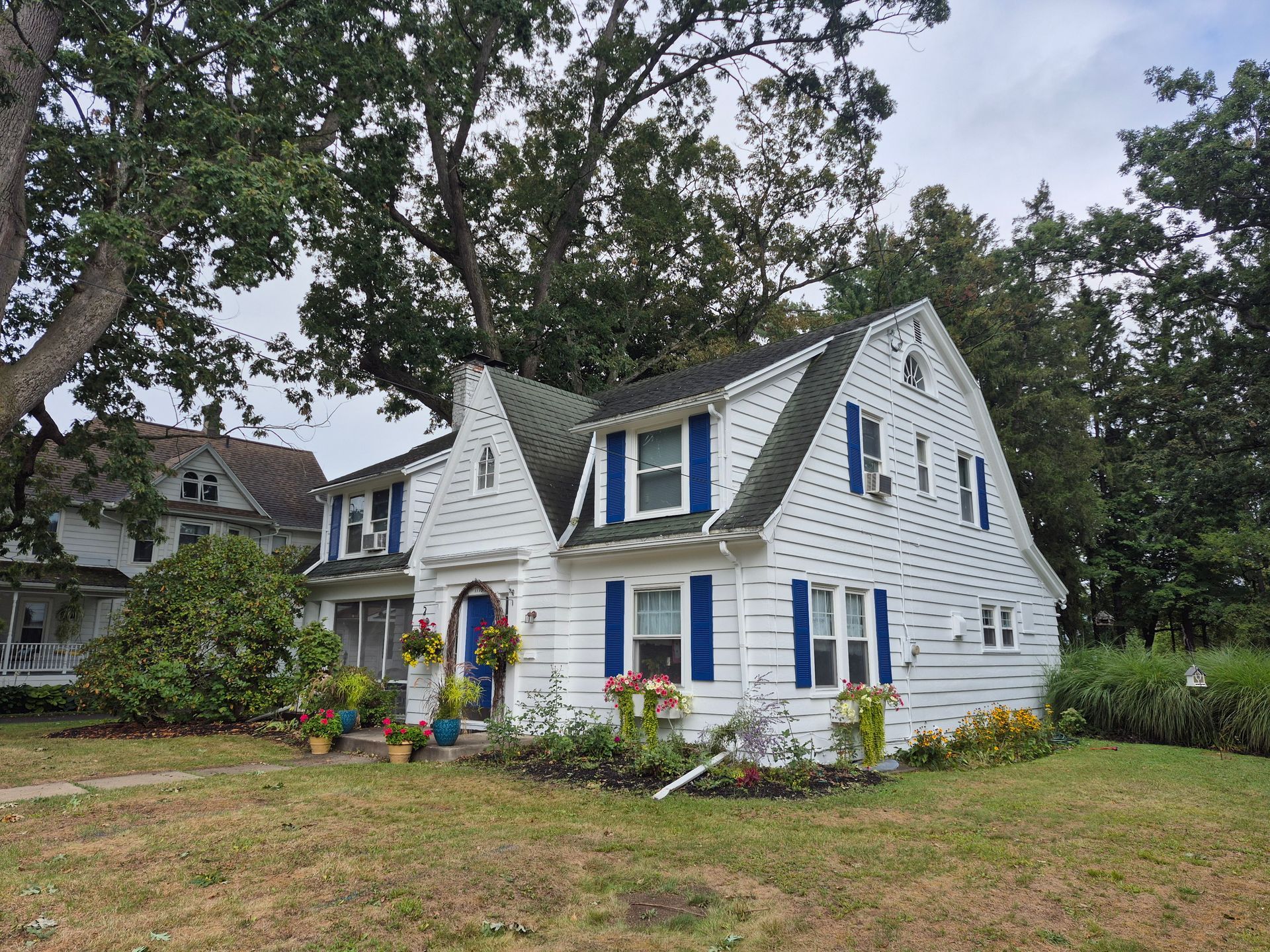 White house with blue shutters, green roof, and flower boxes; trees in the background.