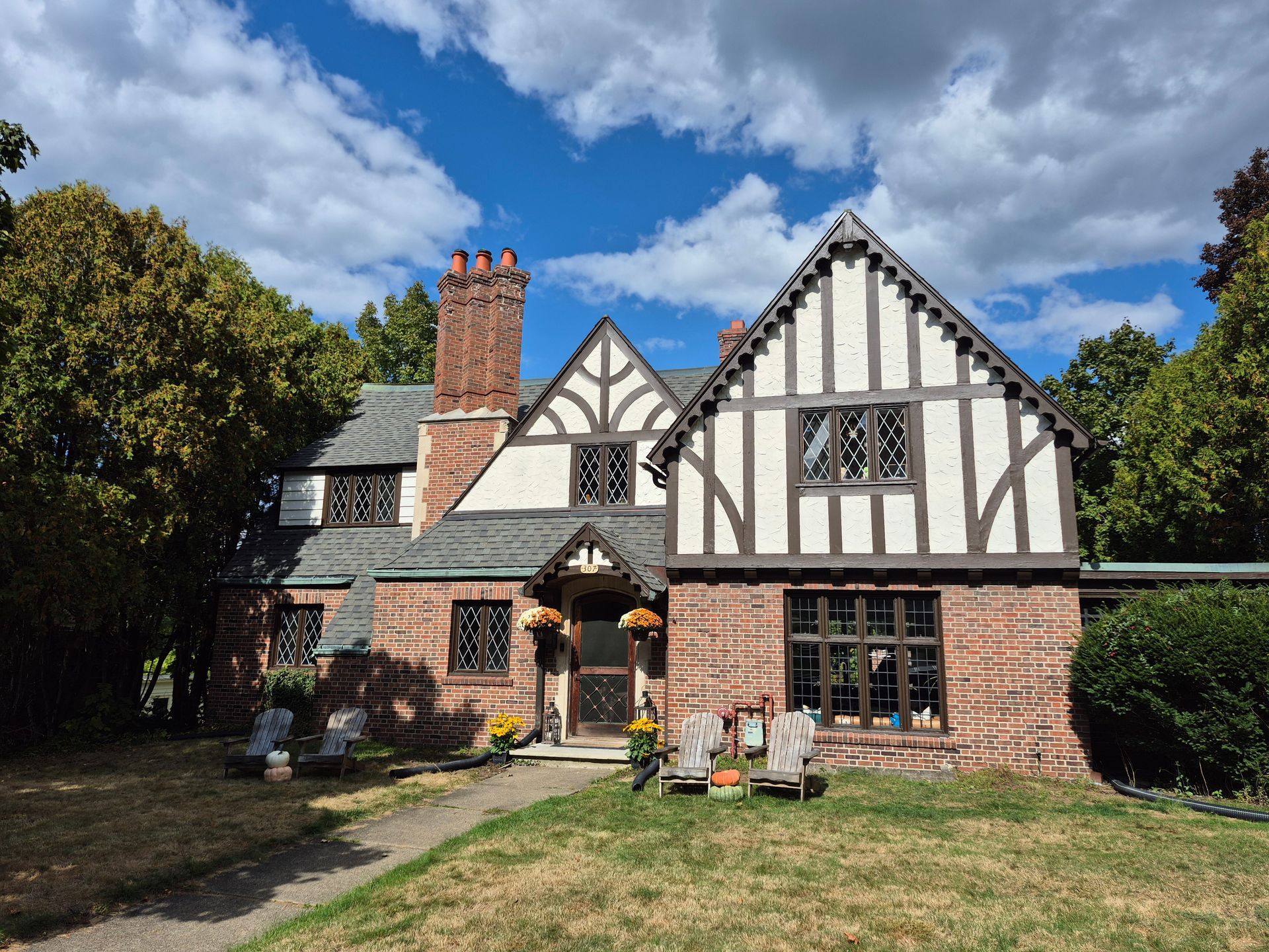 Brick Tudor-style house with brown trim and a chimney against a blue sky with clouds.