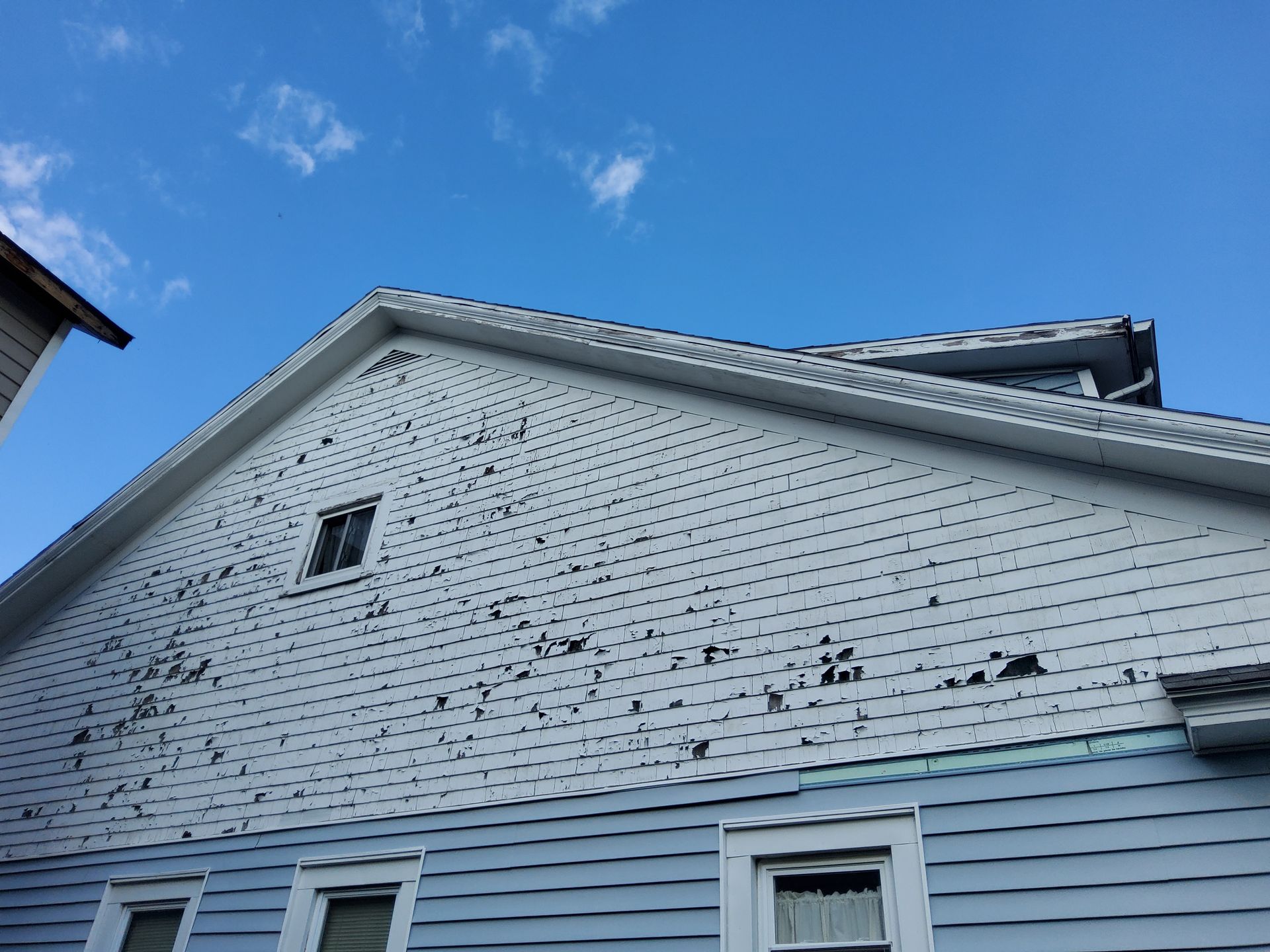 Blue house with peeling paint on siding, against a bright blue sky with white clouds.