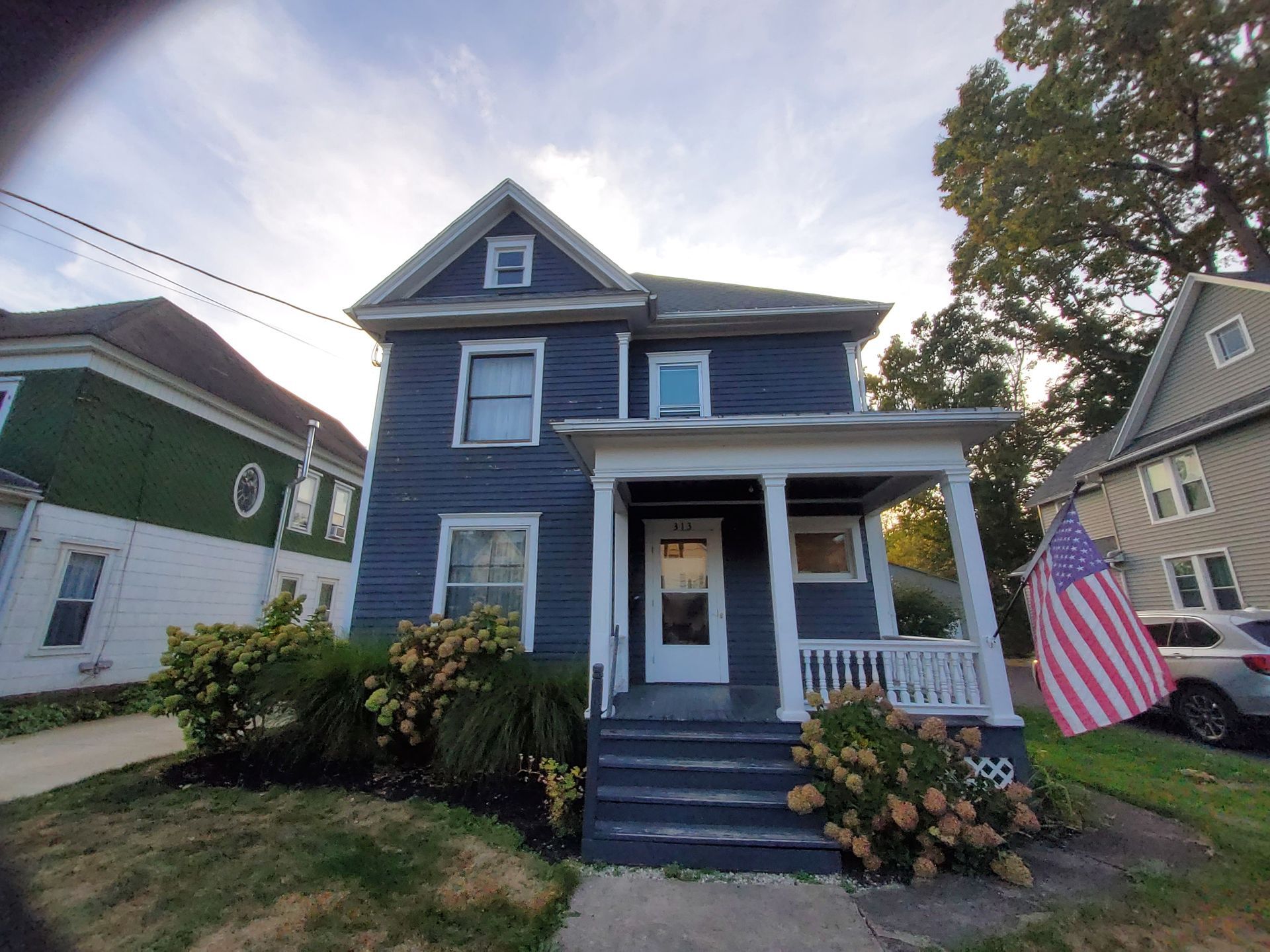 Blue house with a porch and American flag on the right.