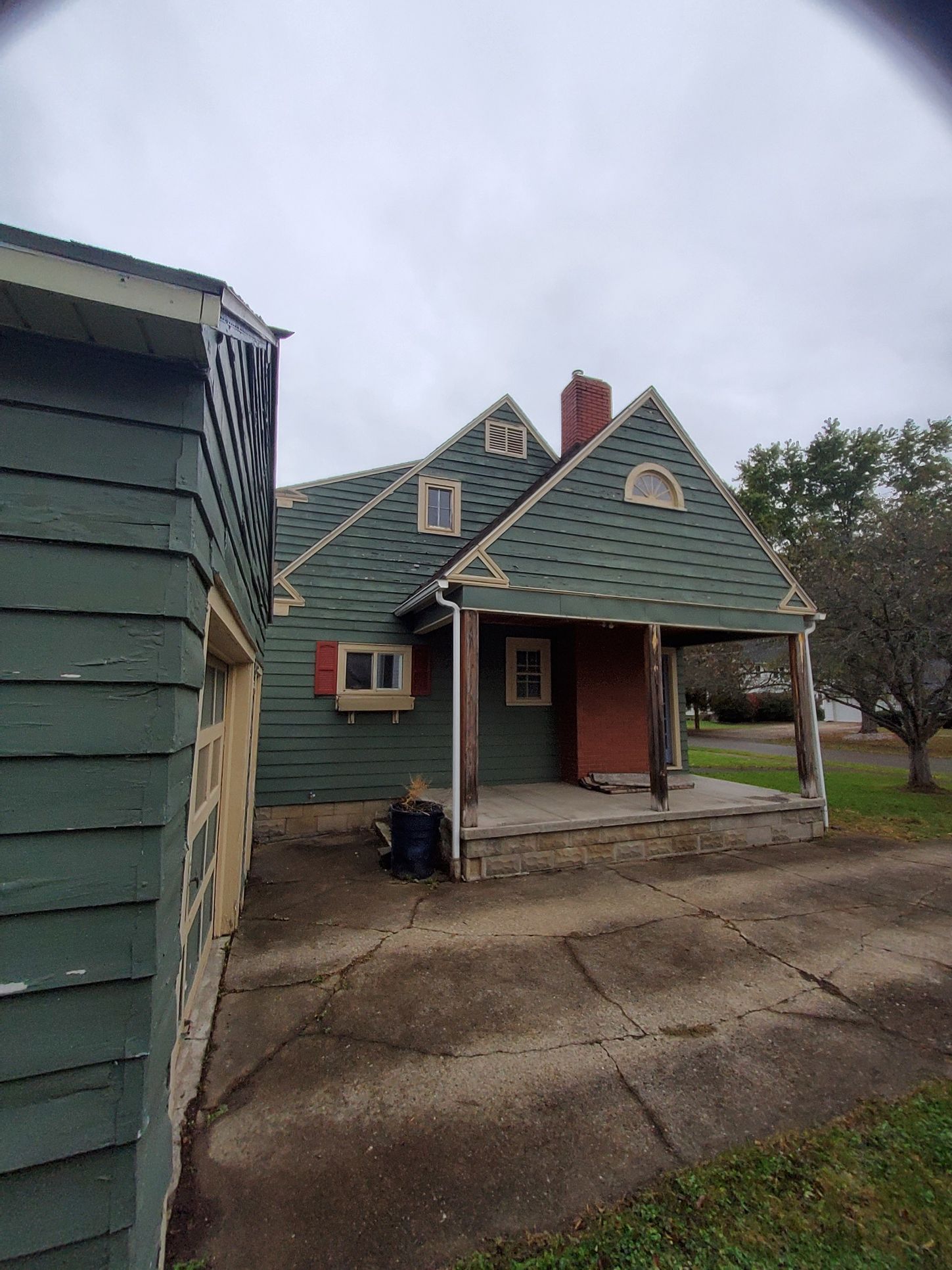 Green house with a porch and red door on a cloudy day. Concrete driveway. Garage on the left.