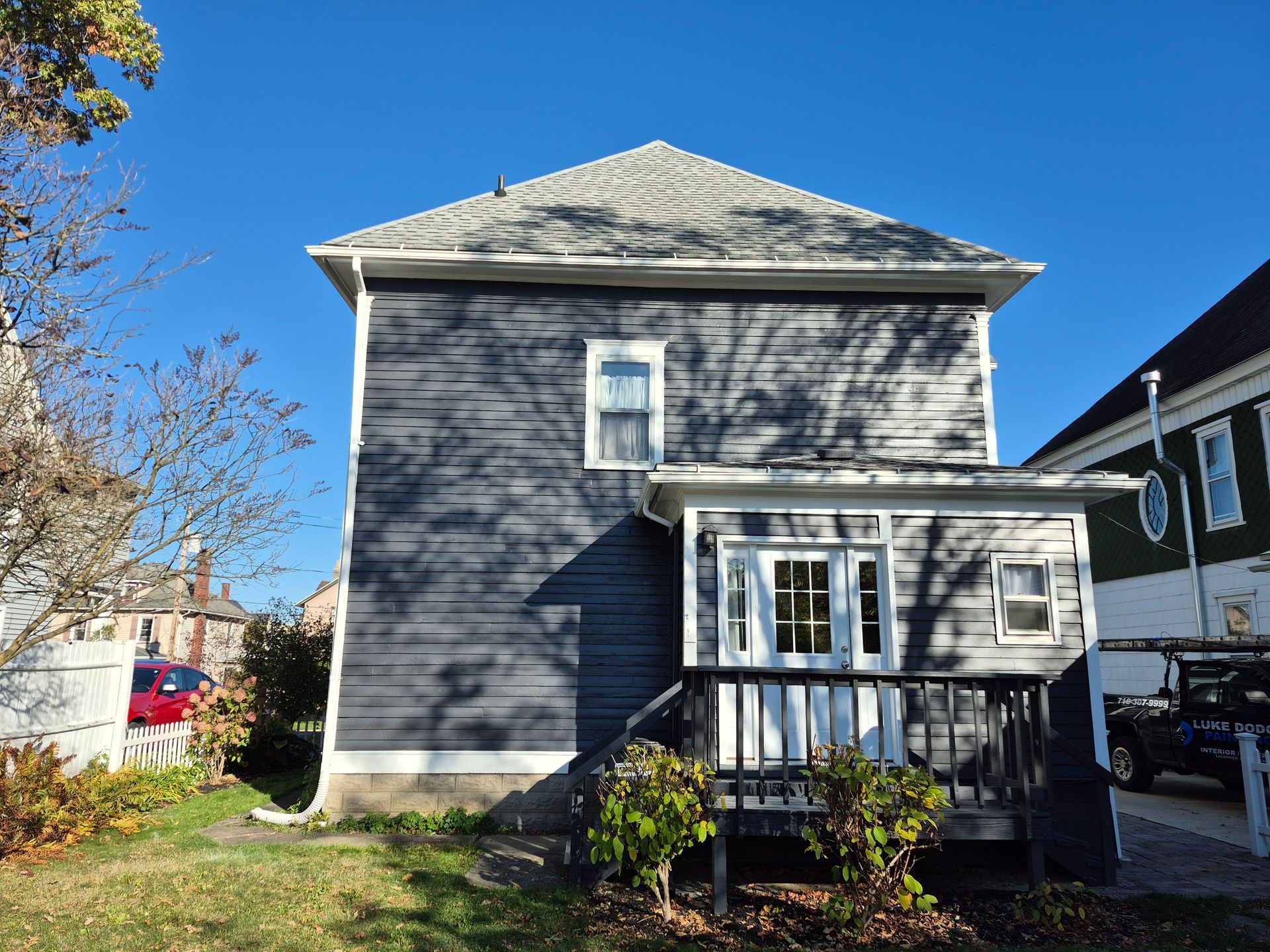 Back view of a two-story blue house with porch and deck, set against a clear sky.