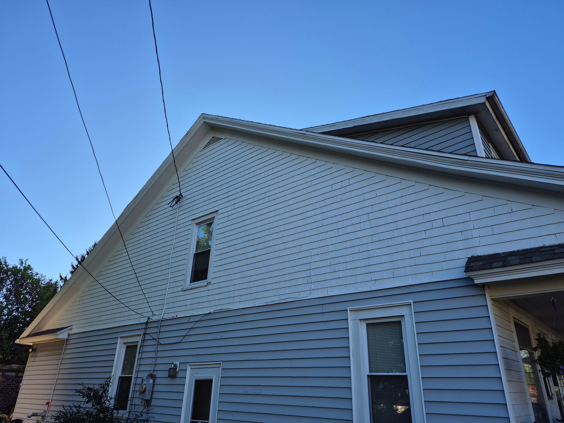 Side view of a two-story house with blue siding, visible windows, and power lines against a clear sky.