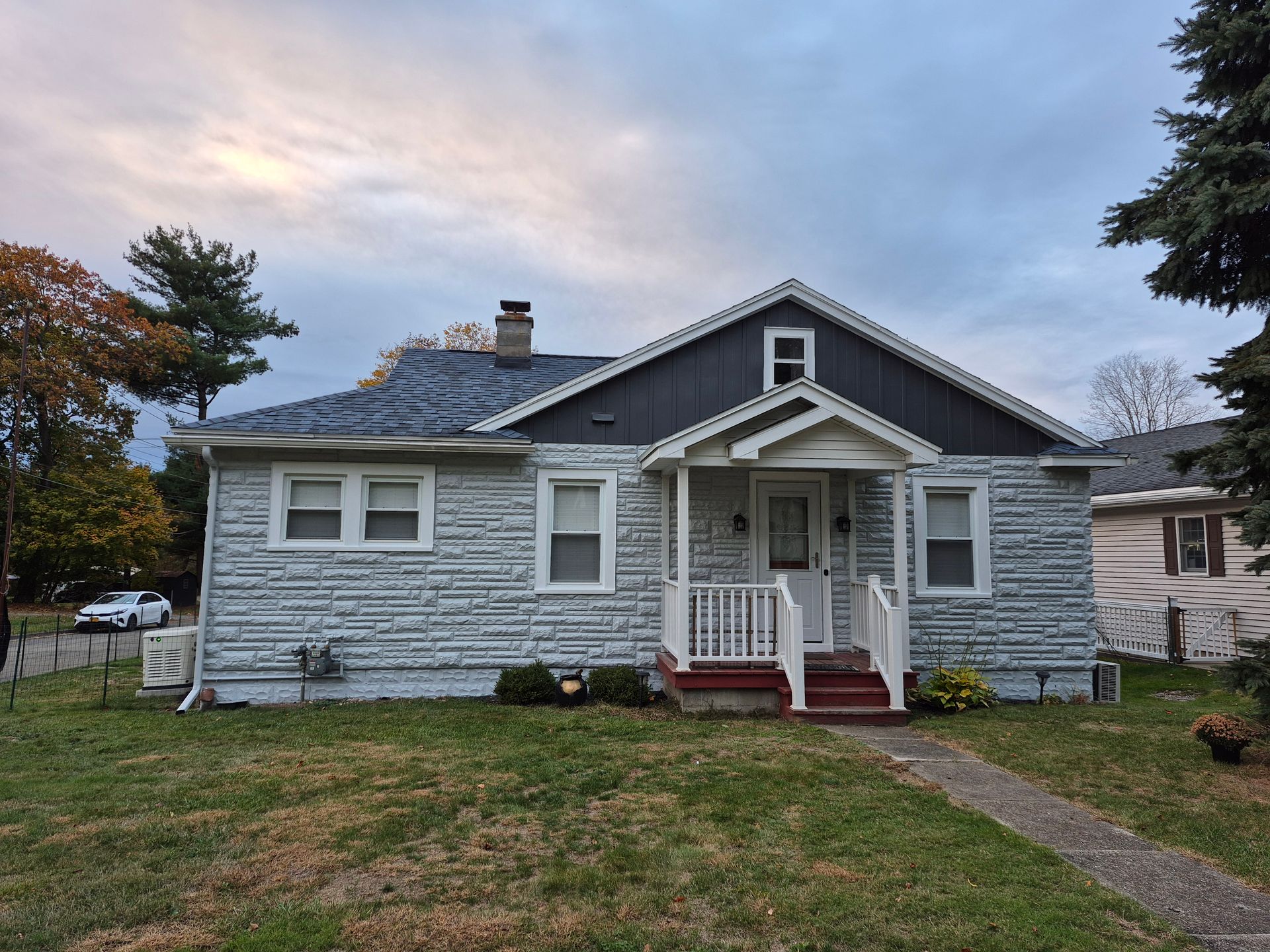 A small, one-story house with gray textured siding and a red front step, under a cloudy sky.