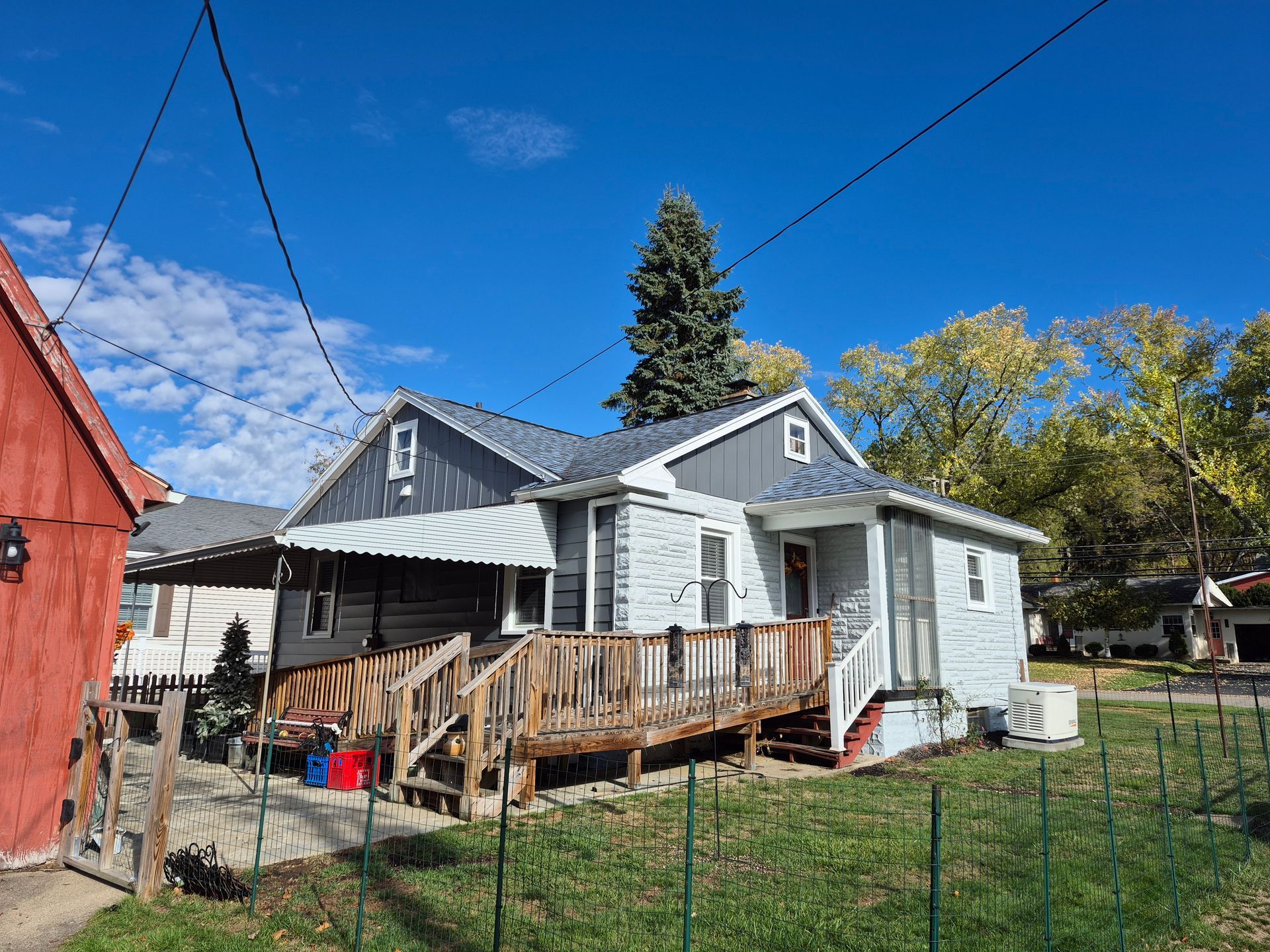 Gray house with wooden porch and awning, bright blue sky in background.