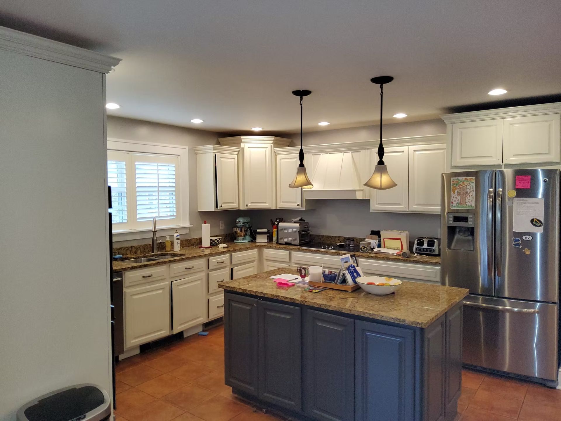 Kitchen with white cabinets, blue island, stainless steel fridge, and pendant lights.