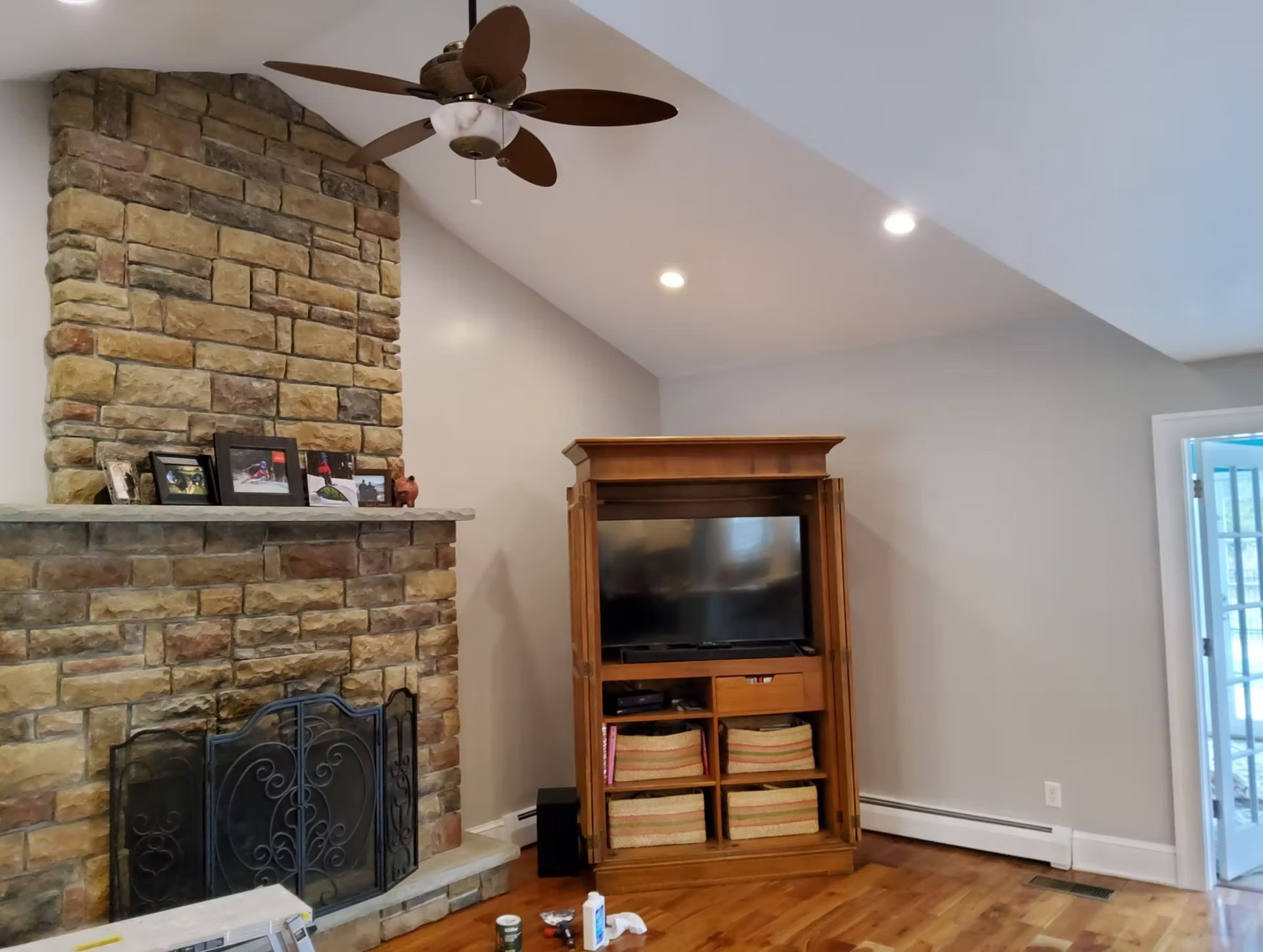 Living room with a stone fireplace, TV cabinet, wood floor, and angled ceiling.