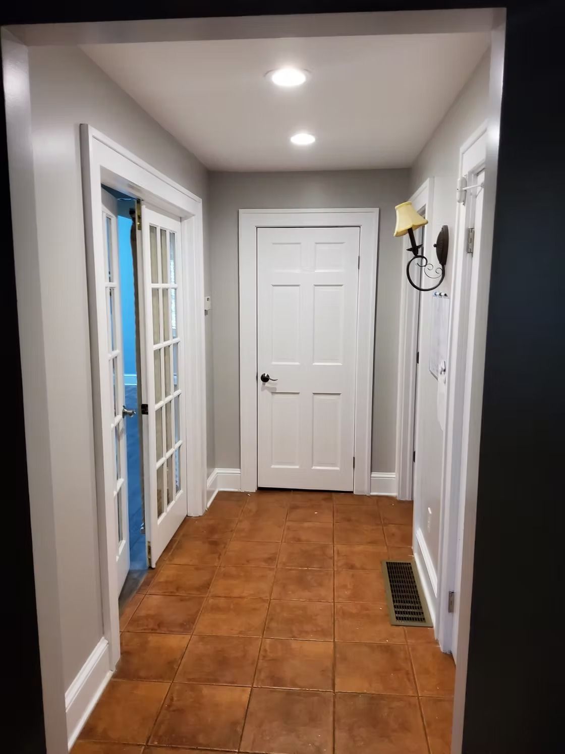 Narrow hallway with brown tile floor, white doors, and gray walls.